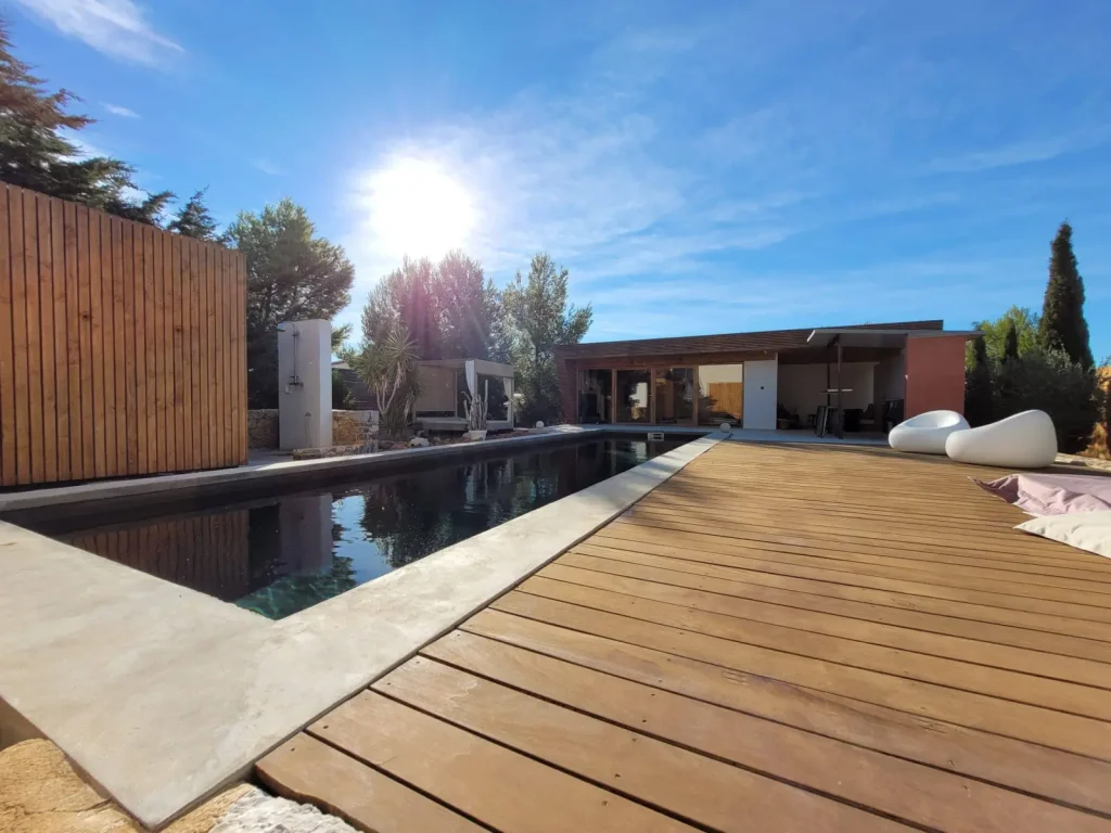 Pool at 4U Bed&Spa in the sunshine, with wooden deck, white poufs and the pool house beyond