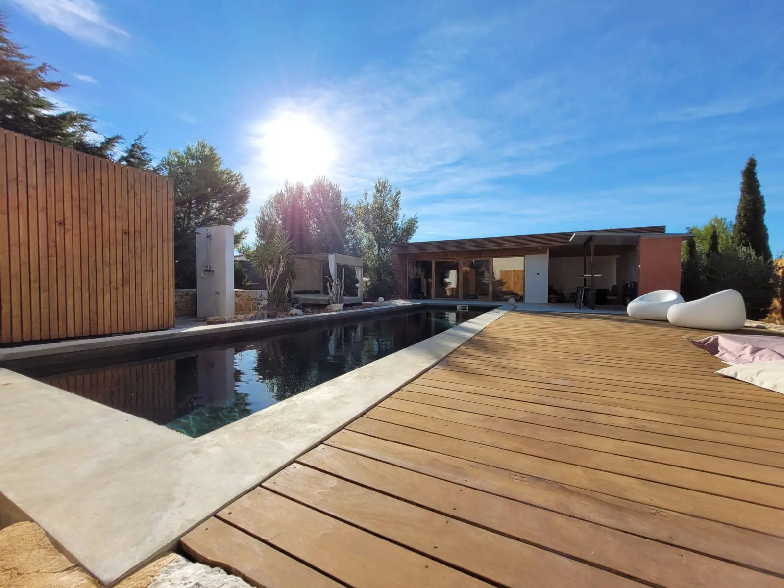 Pool at 4U Bed&Spa in the sunshine, with wooden deck, white poufs and the pool house beyond