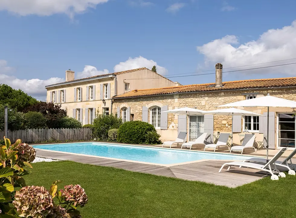 Piscine de la Bastide Margaux bordée de transats et de parasols blancs devant la longère en pierre claire