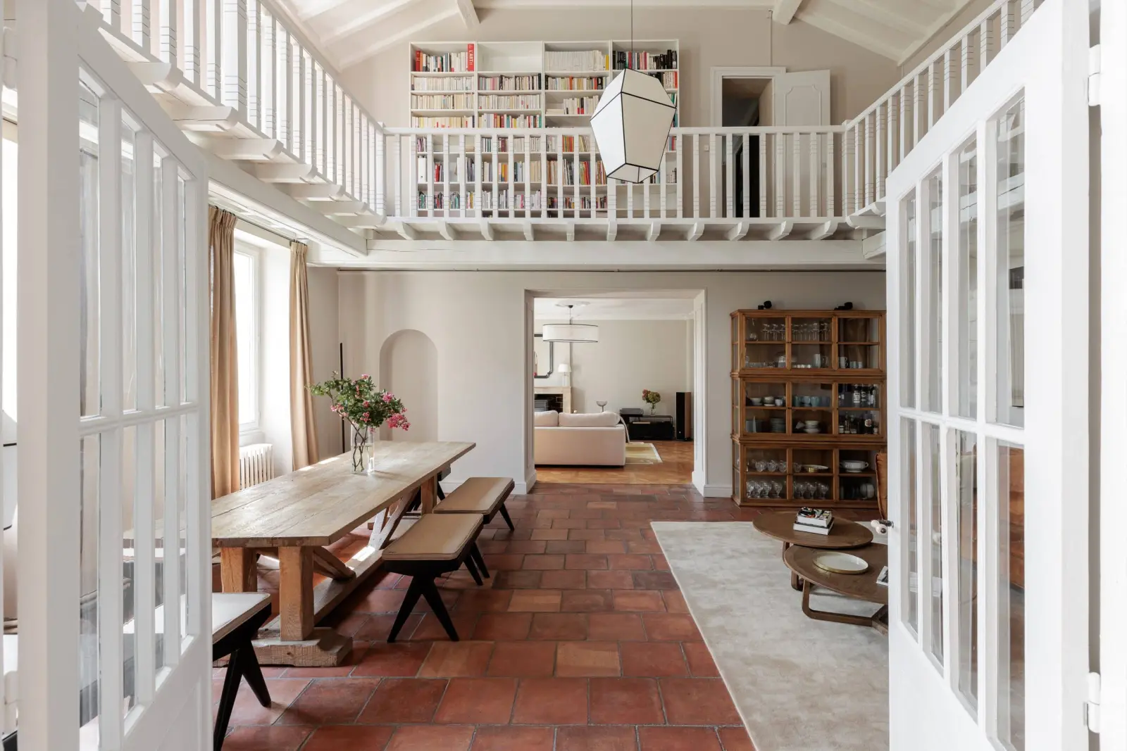Large terracotta-tiled room with a farmhouse table, white wooden gallery and bookshelves, La Bastide de Margaux