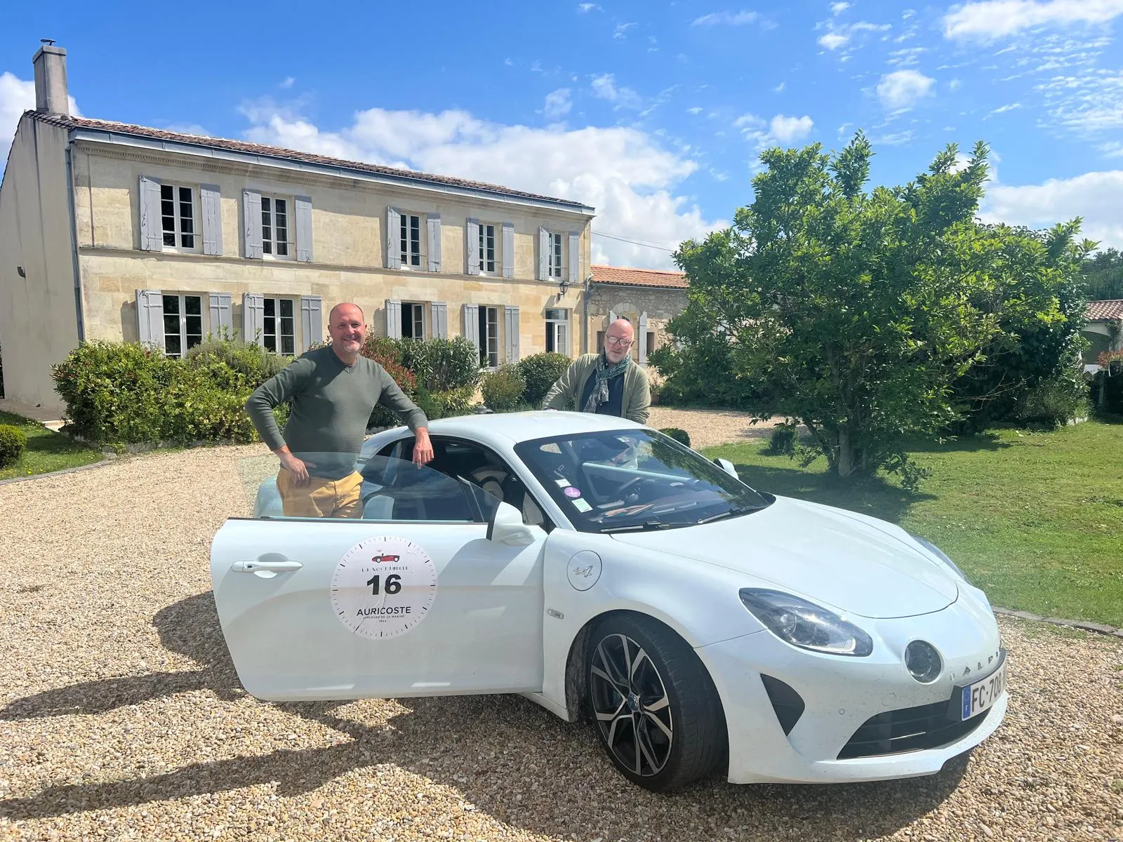 Two men by a white sports car parked on the gravel in front of La Bastide de Margaux