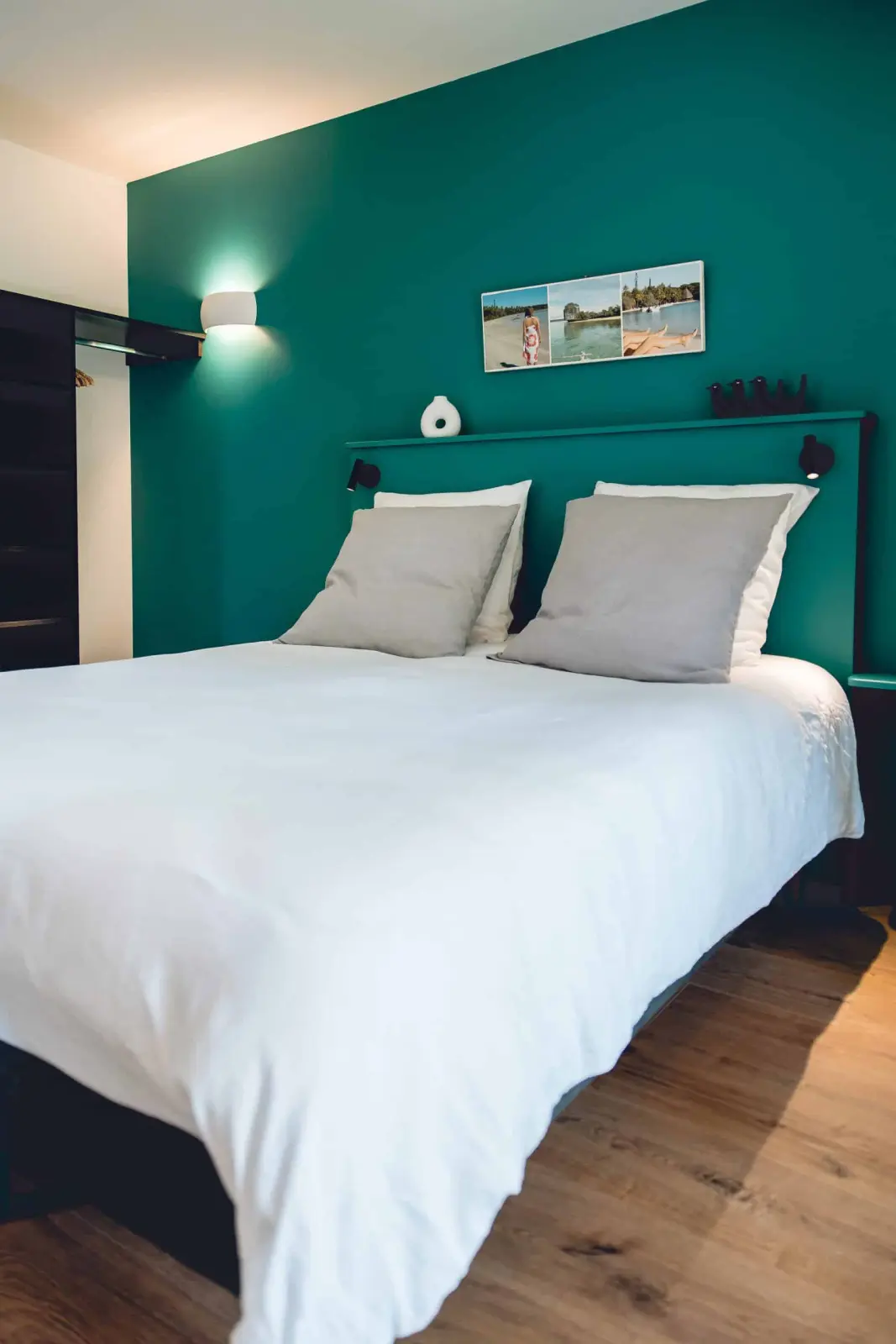 Bedroom at Bread et Couette with a teal wall, large white bed, grey cushions and light wooden floor