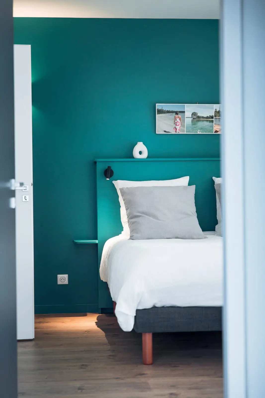 Teal-walled bedroom at Bread et Couette seen through the doorway, white bed and beach photos above it