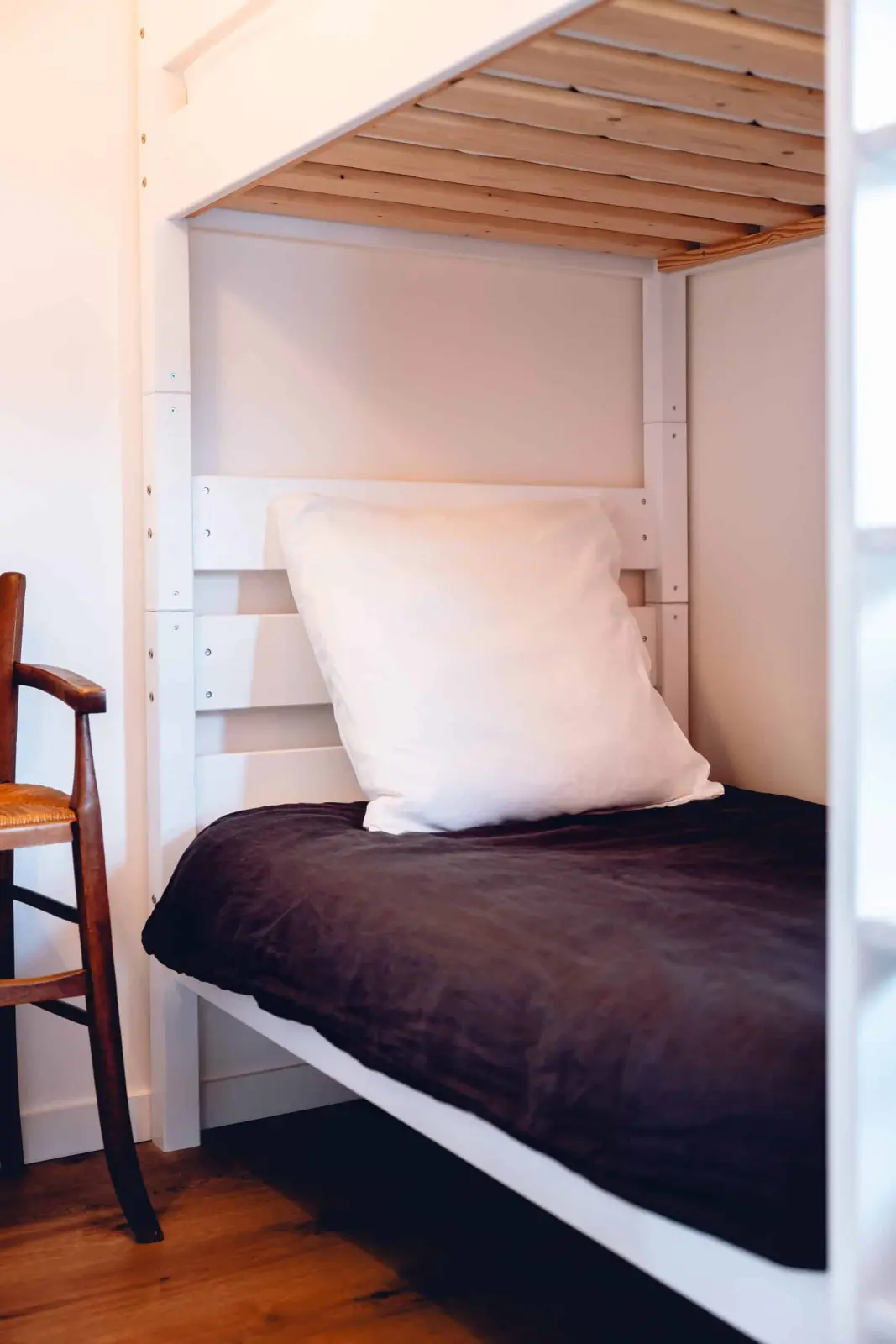 White wooden bunk bed with a plum duvet and white pillow, rush-seat chair alongside, at Bread et Couette