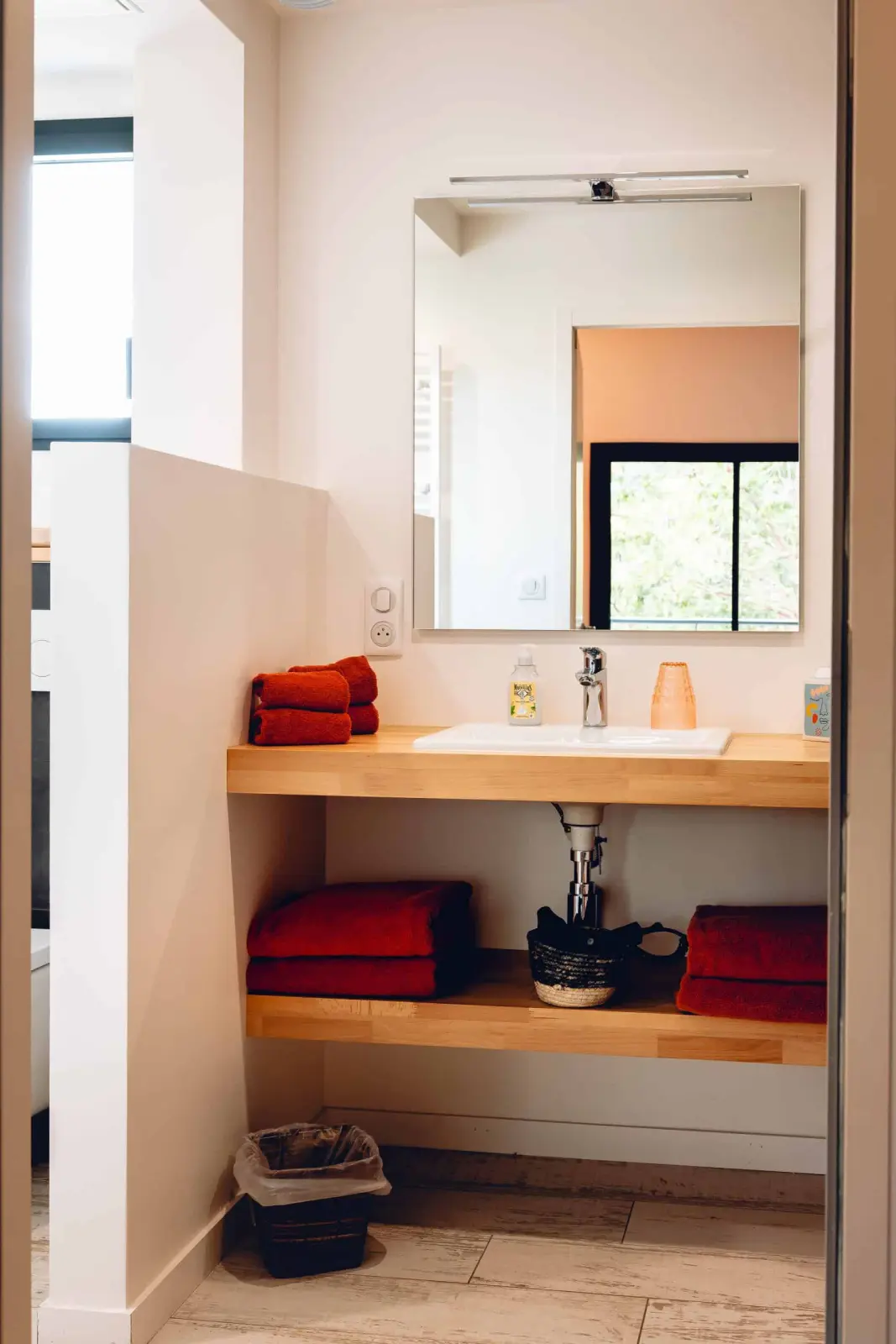 Bathroom at Bread et Couette with a basin on a wooden shelf, red towels and a large mirror