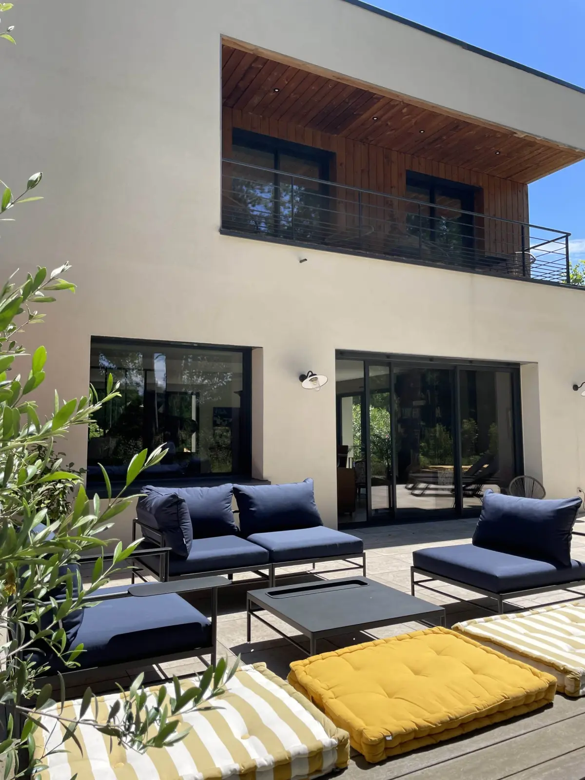 Terrace at Bread et Couette with navy garden sofas and yellow striped cushions below a wood-clad balcony