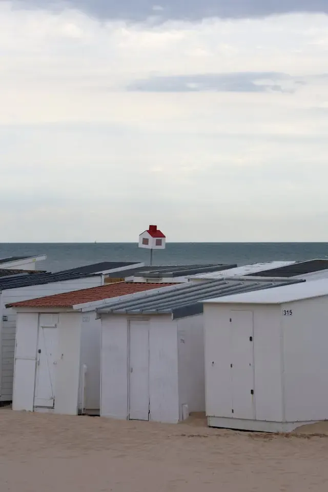 Cabines de plage blanches sur le sable face à la mer, sous un ciel nuageux