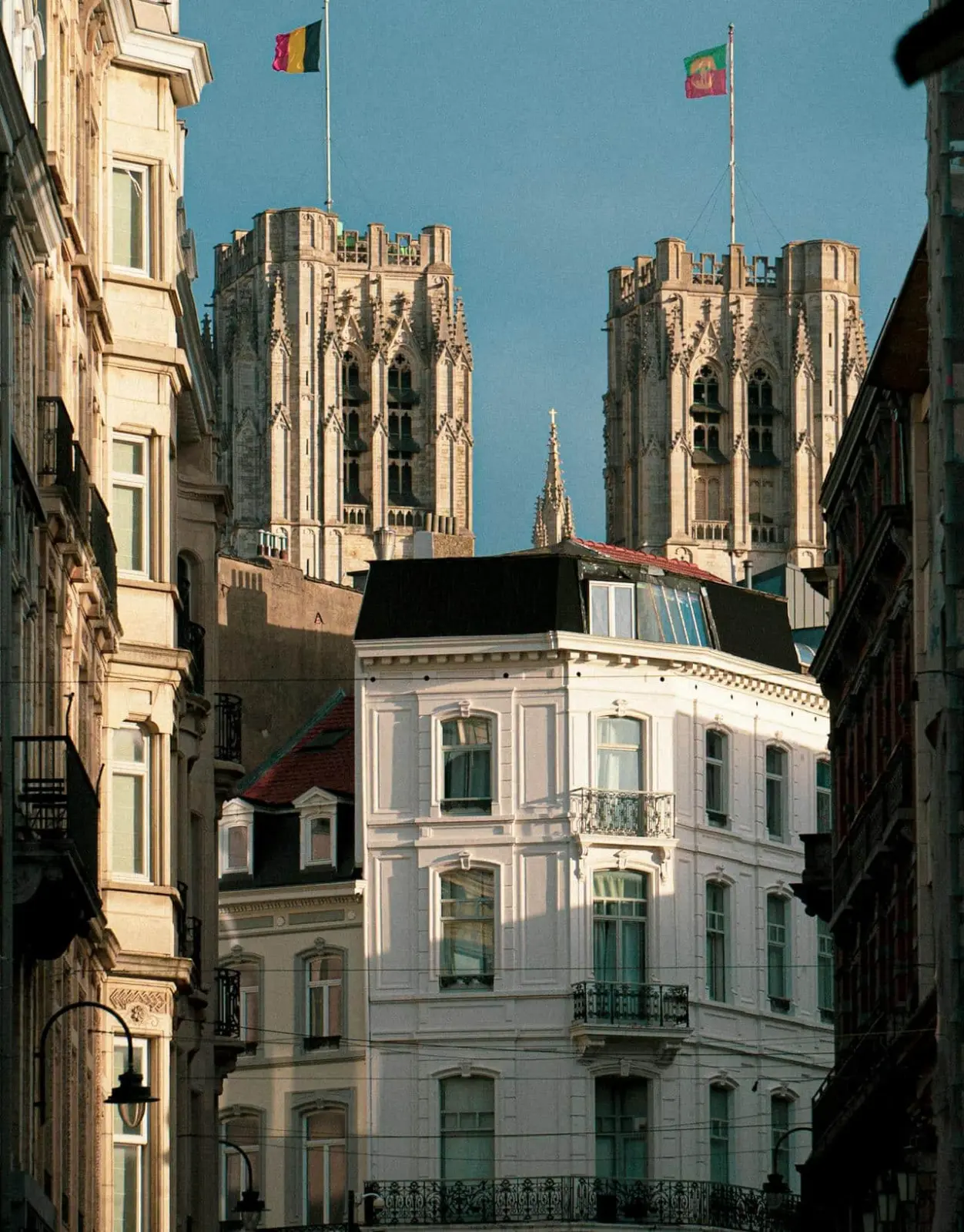 Tours gothiques d'une cathédrale et drapeau belge au-dessus d'un immeuble blanc d'une rue de ville