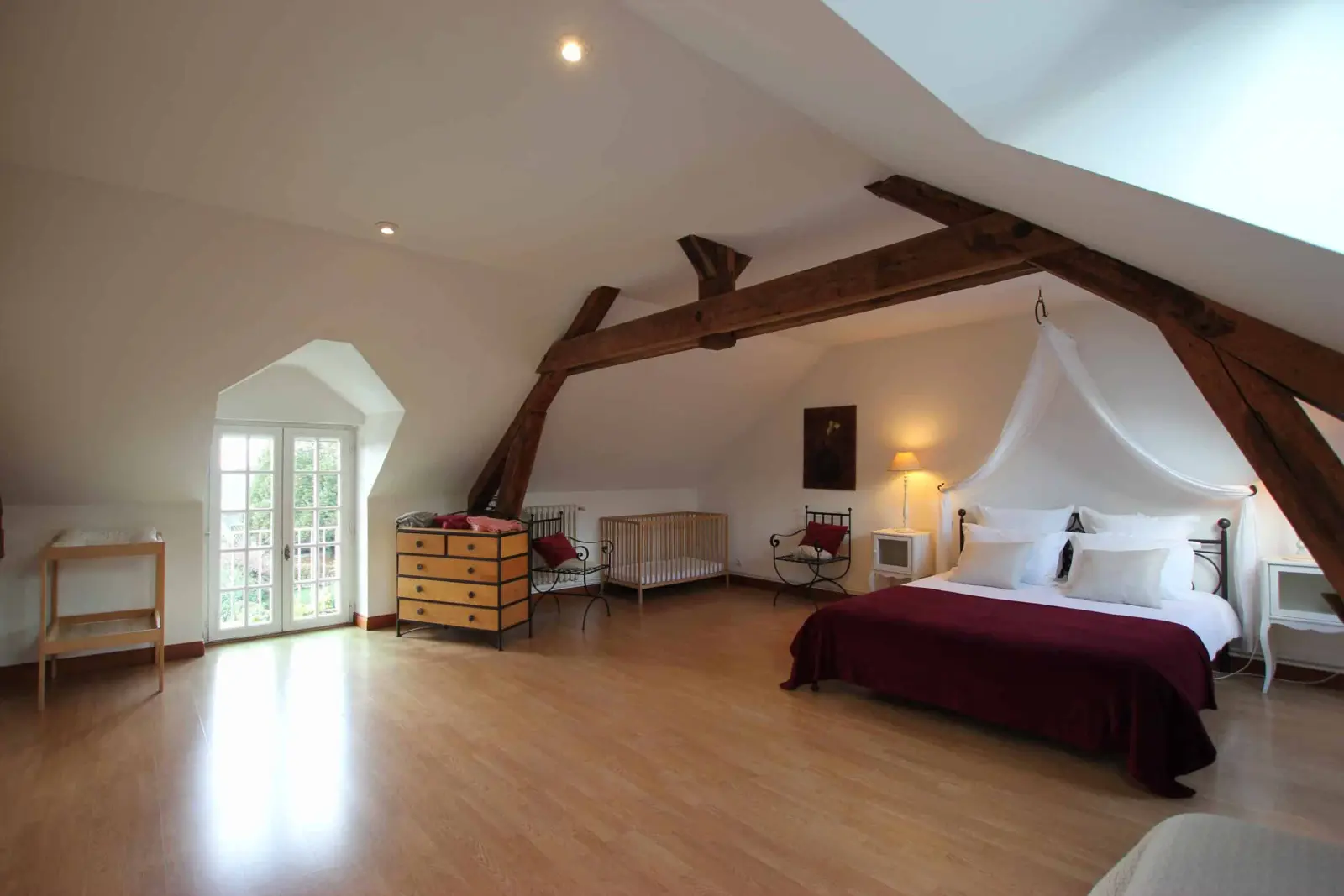 Large attic bedroom in the Hortensias gîte, wooden beams, bed with white canopy and French window
