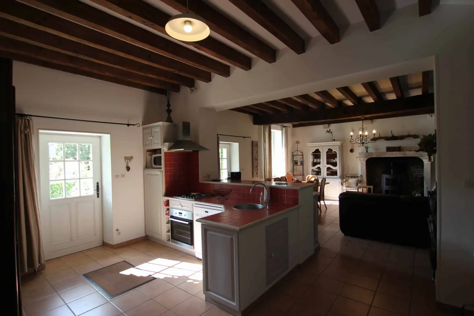 Open kitchen of the Hortensias gîte, terracotta floor, glazed garden door and living room with fireplace