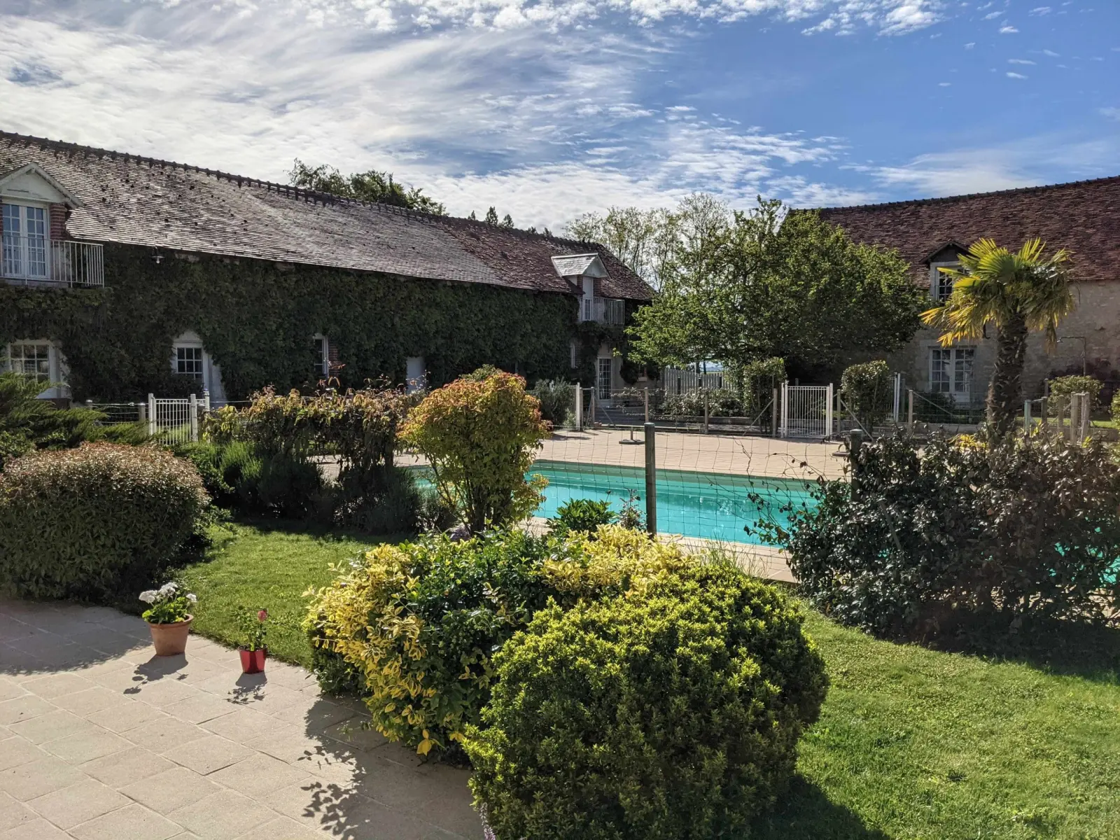 Garden and pool at Domaine de Champouteau, paved terrace, clipped shrubs and ivy-covered buildings