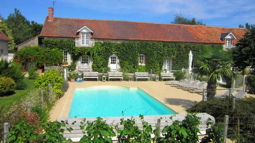 Pool at Domaine de Champouteau in front of the long house covered in Virginia creeper, with benches and loungers