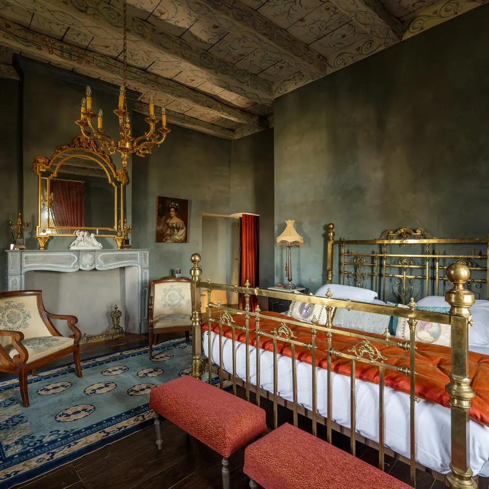 Room at Château de Canac with brass bed, painted ceiling, fireplace, gilt mirror and red benches