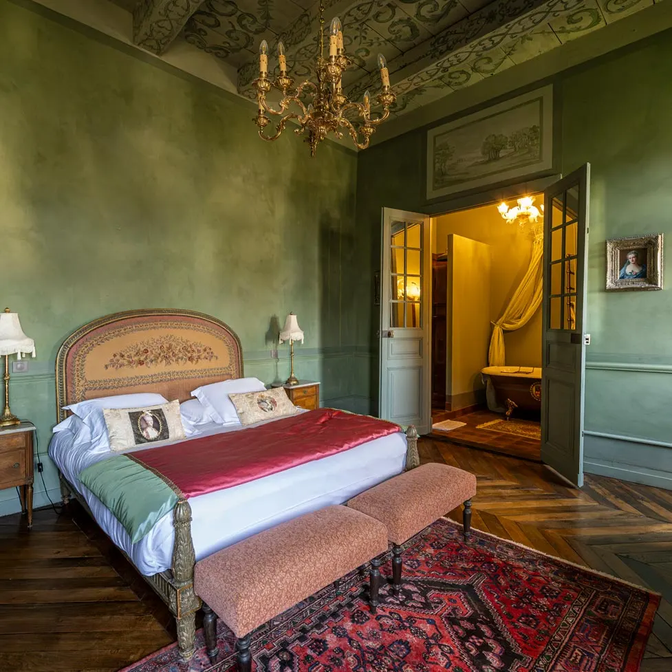 Green bedroom at Château de Canac with double bed, gilt chandelier and antique rug, door open onto the bathtub