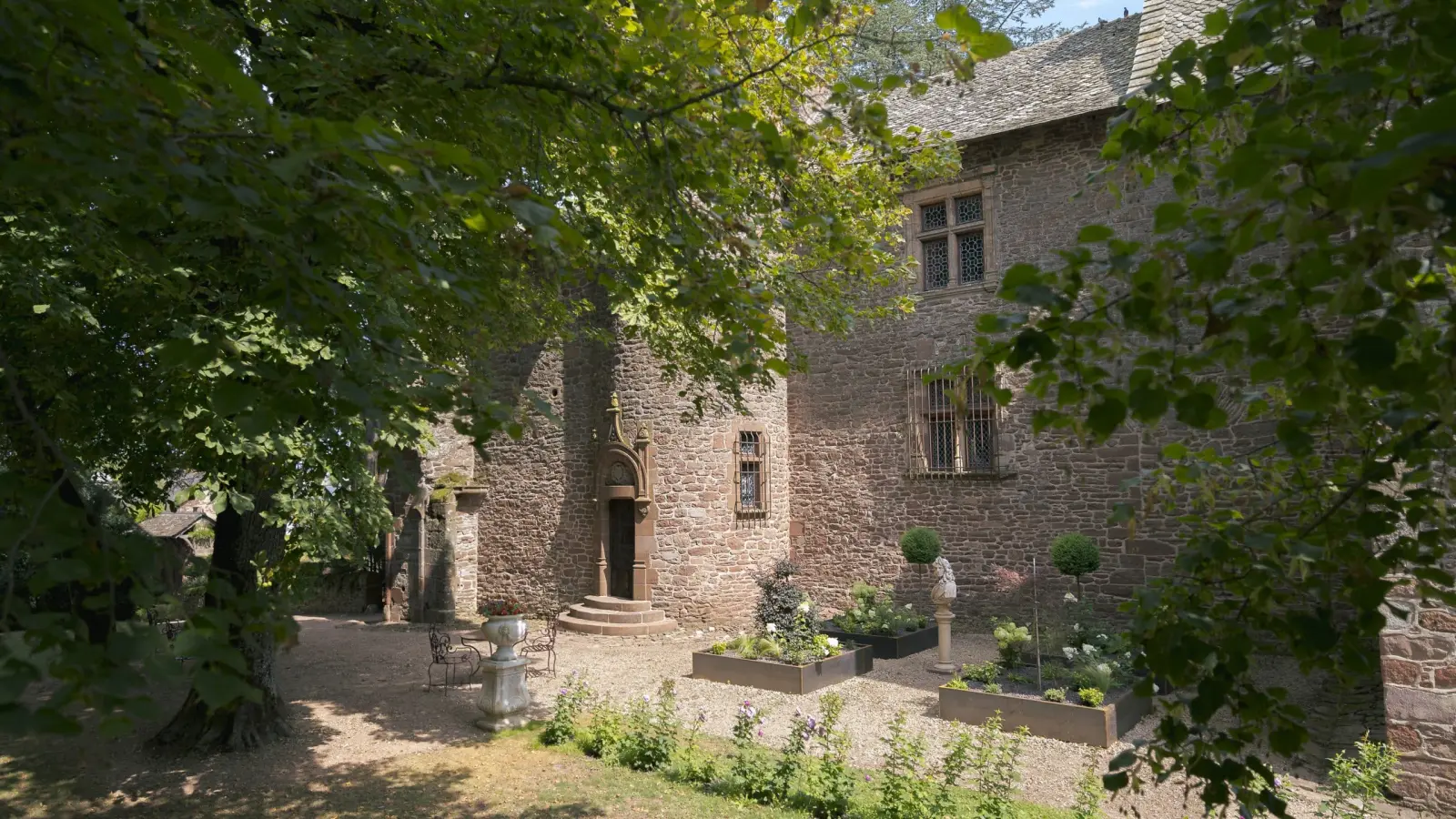Gravel courtyard in front of the stone façade of Château de Canac, carved doorway and planters, under trees