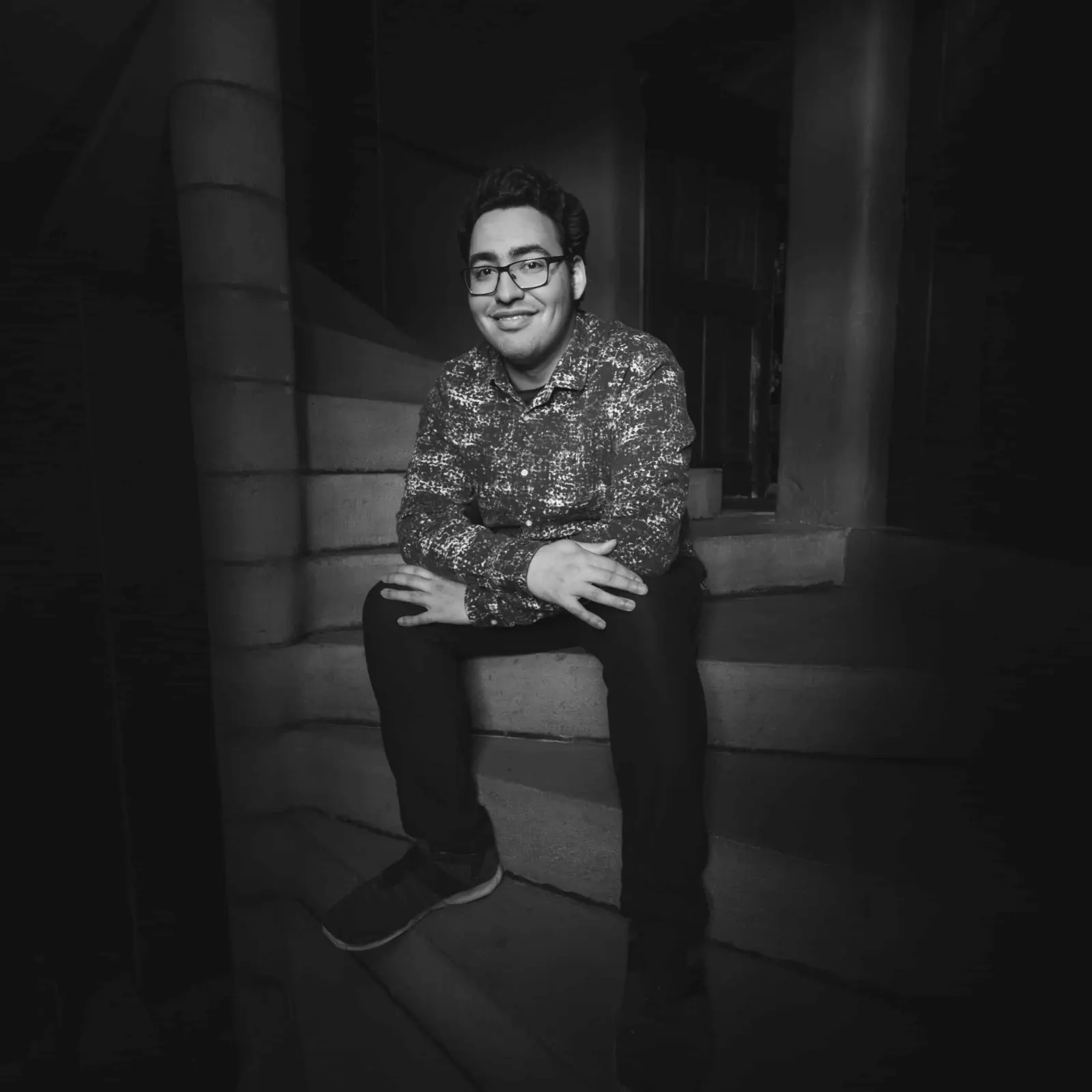 Black-and-white portrait of the host of Château de Canac, smiling, seated on a stone staircase
