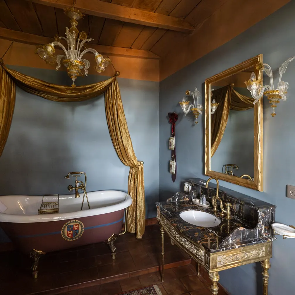 Bathroom at Château de Canac with clawfoot bath, gold drapes, glass chandelier and marble washstand