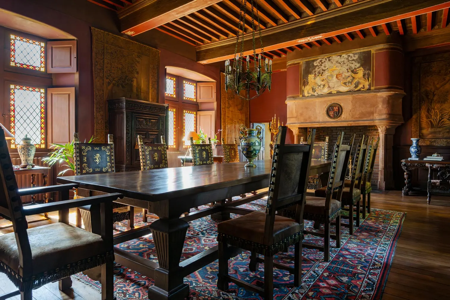 Dining room at Château de Canac: long wooden table, carved chairs, large fireplace and stained-glass windows