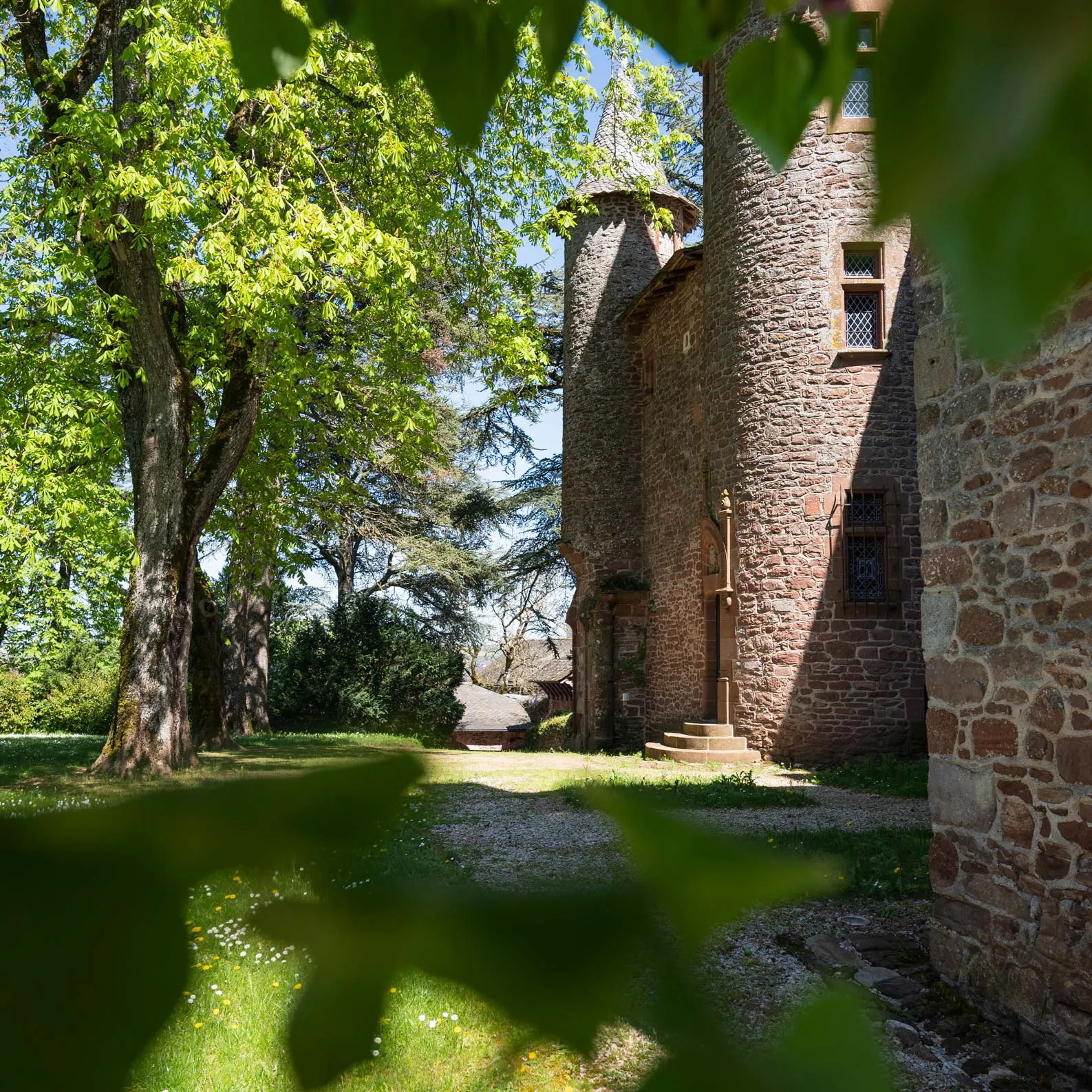 Stone towers of Château de Canac at the end of a path, between lawn and tall trees