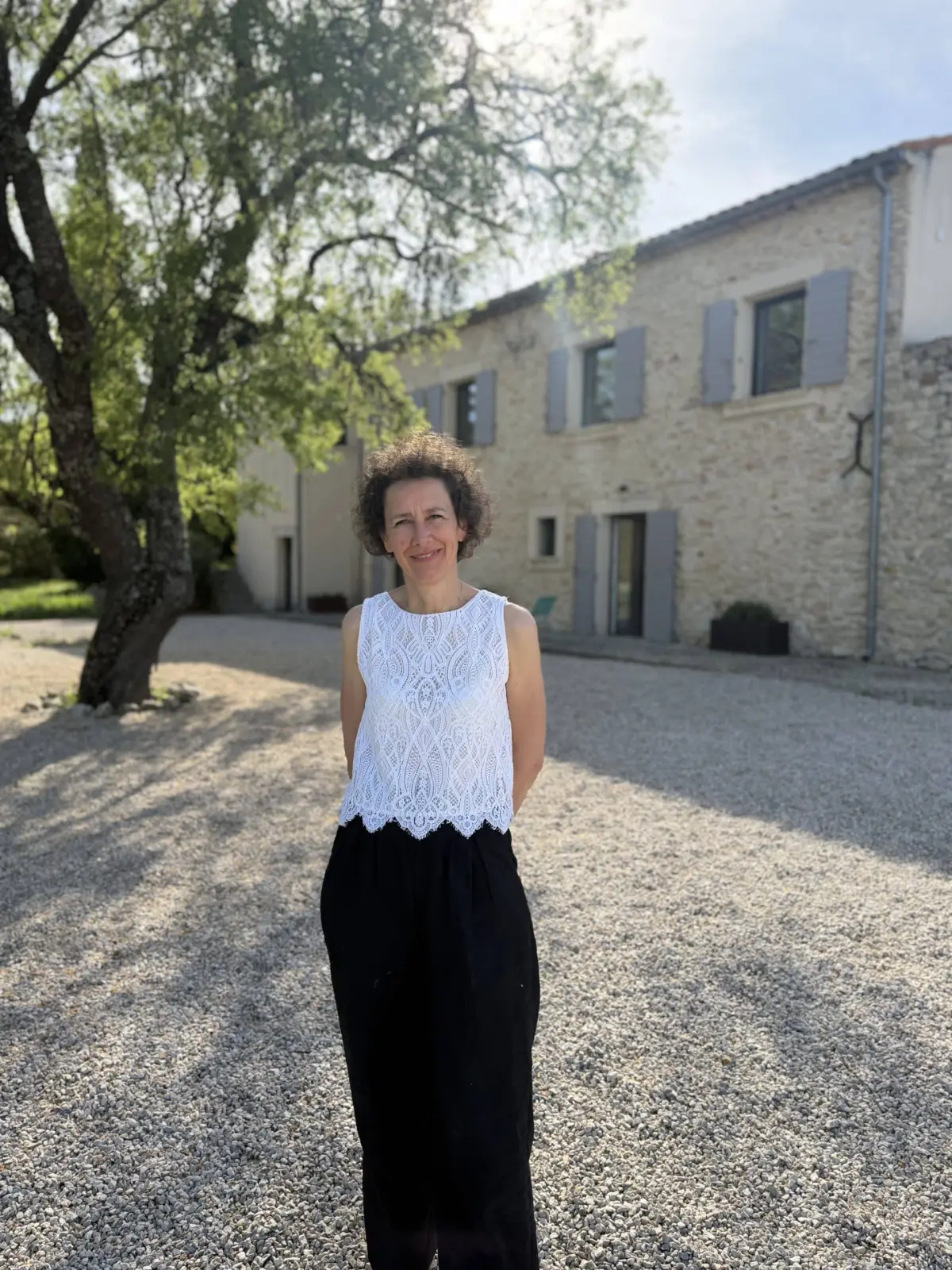 Caroline, host of Chut ! c'est ici, standing in the gravel courtyard in front of the stone house