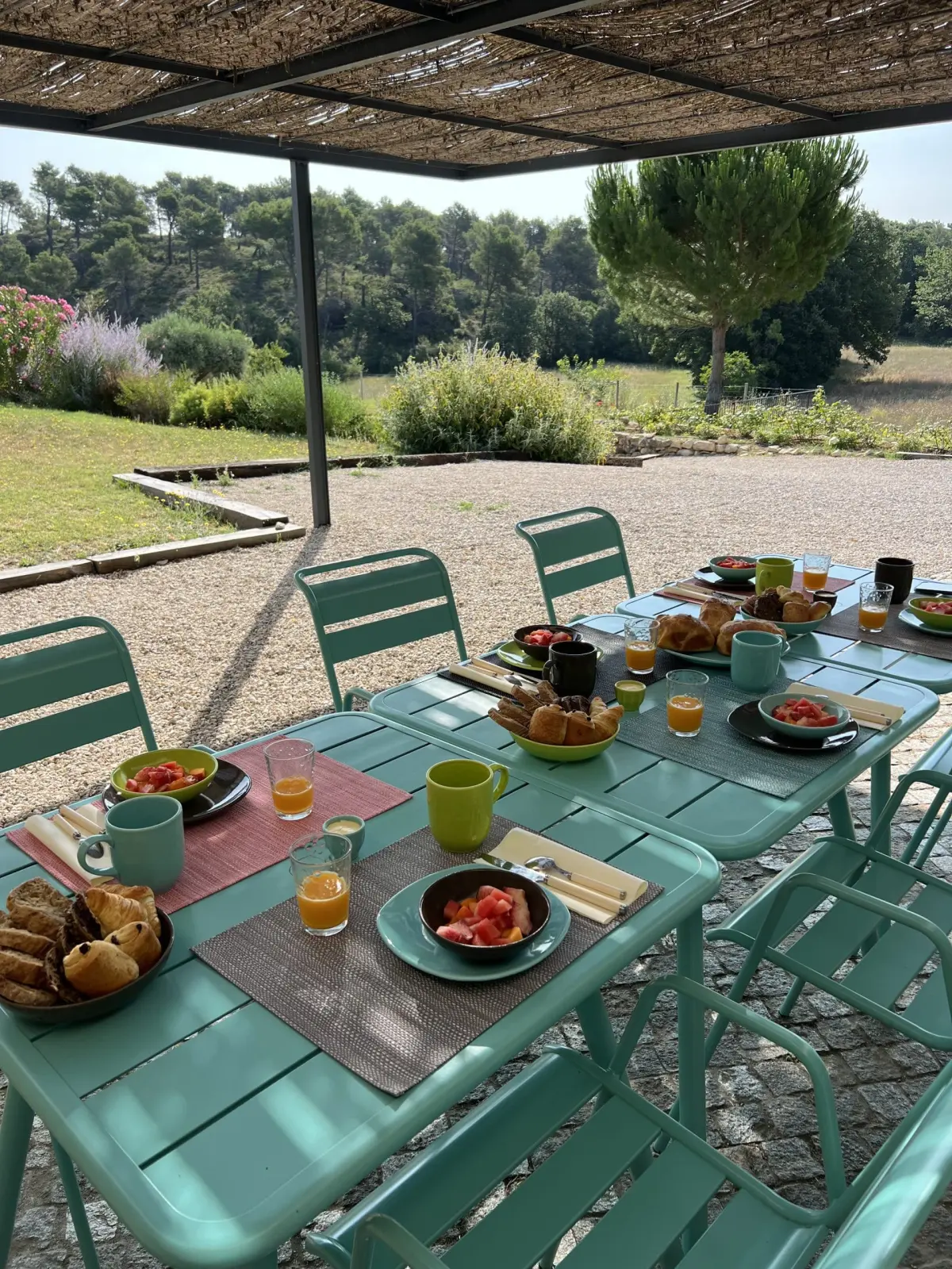 Breakfast under the pergola at Chut ! c'est ici: green tables, pastries, juice and watermelon