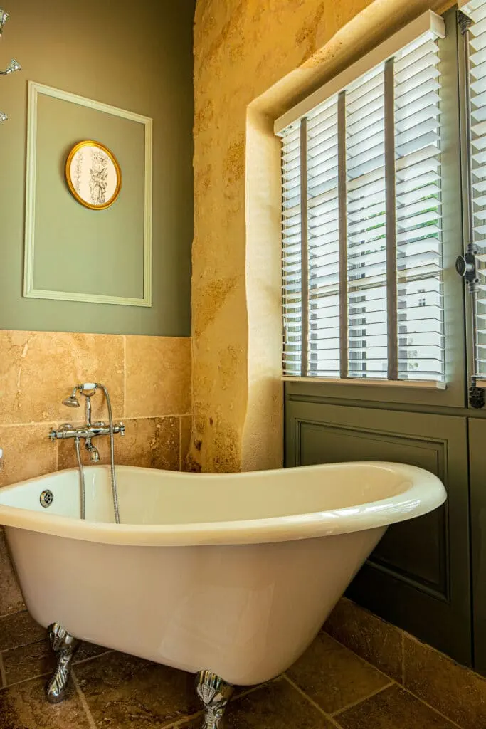 Clawfoot bath in the Côté Campagne suite at Clos Marcamps, stone wall and window with blinds