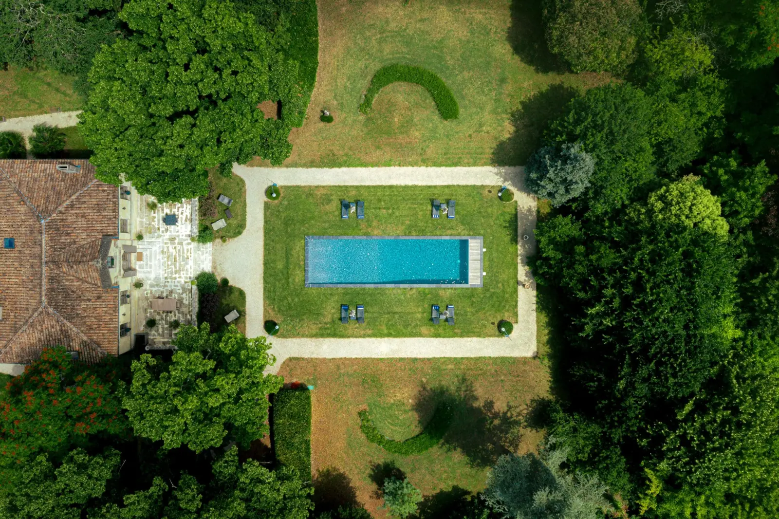 Aerial view of the swimming pool at Clos Marcamps surrounded by lawn, loungers and tall trees