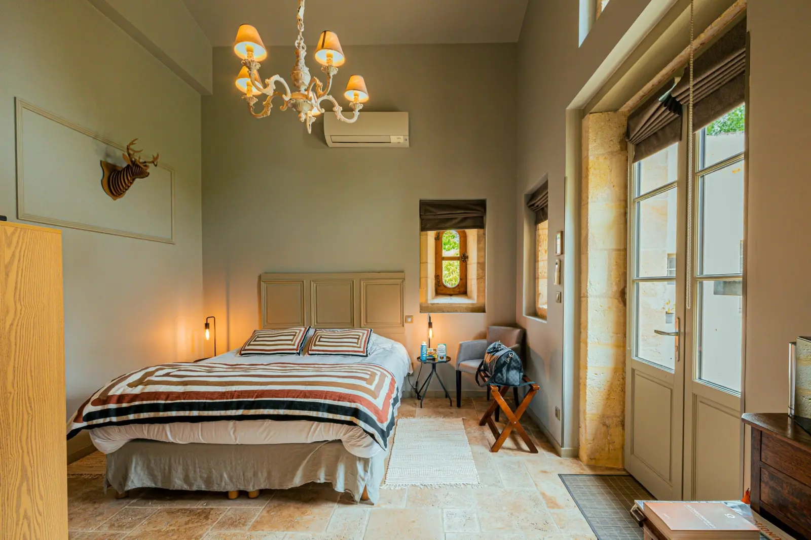 Côté Jardin room at Clos Marcamps with striped throw, chandelier, wooden stag head and stone floor