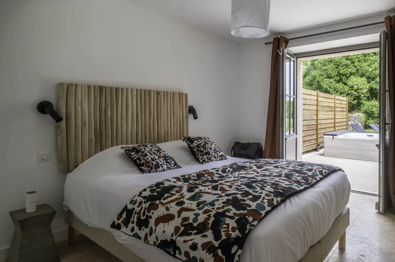 Bedroom in the Clos Marcamps duplex with log headboard, French door open onto a terrace with hot tub