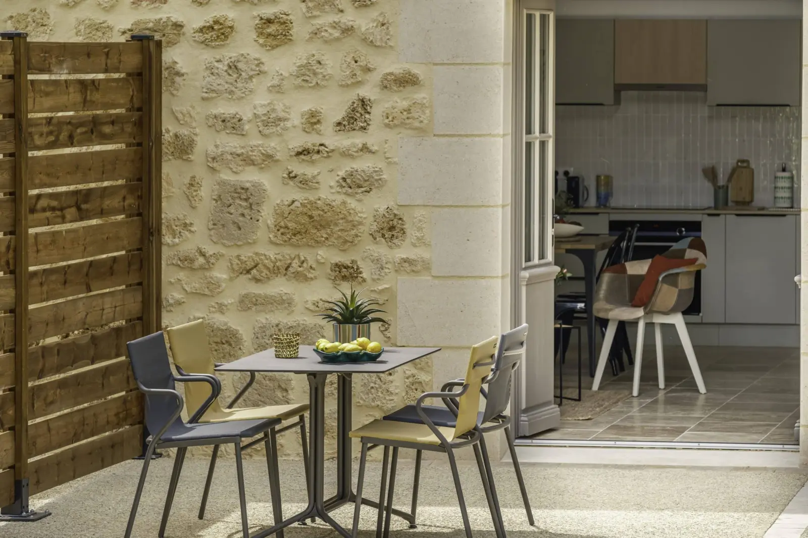 Terrace of the Clos Marcamps duplex, table and chairs by a stone wall, door open onto the kitchen