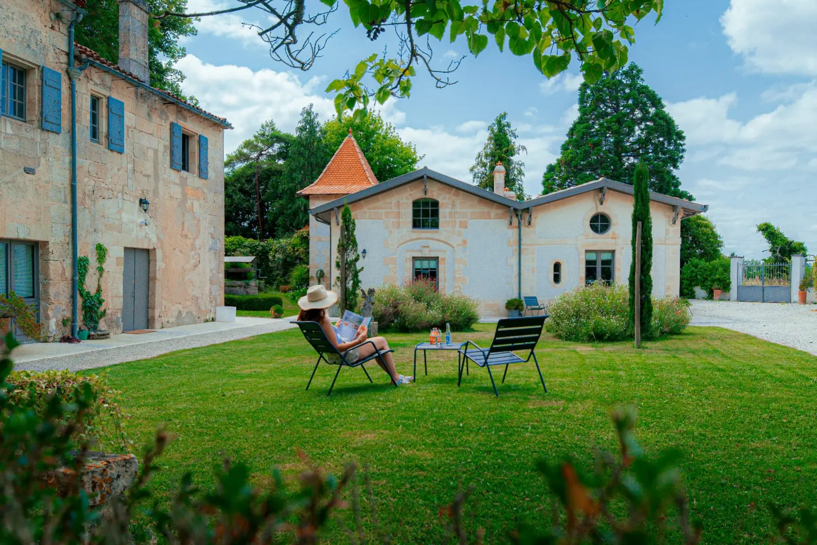 Woman in a hat reading on a lounger on the lawn in front of the stone buildings of Clos Marcamps