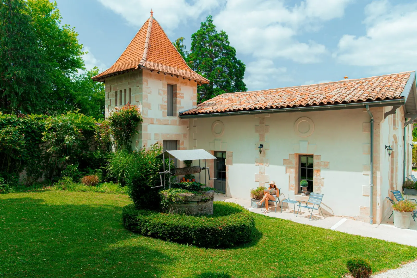 Pigeonnier au toit pointu en tuiles et bâtiment clair du Clos Marcamps, pelouse et puits fleuri