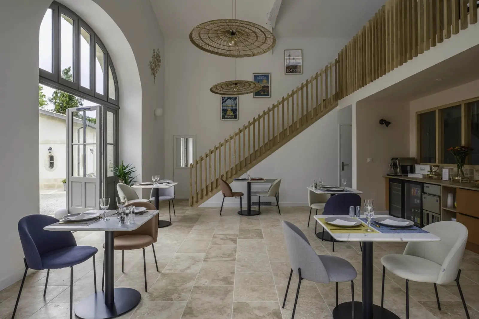 Shared room at Clos Marcamps with arched window, wooden staircase, wicker pendant lights and laid tables