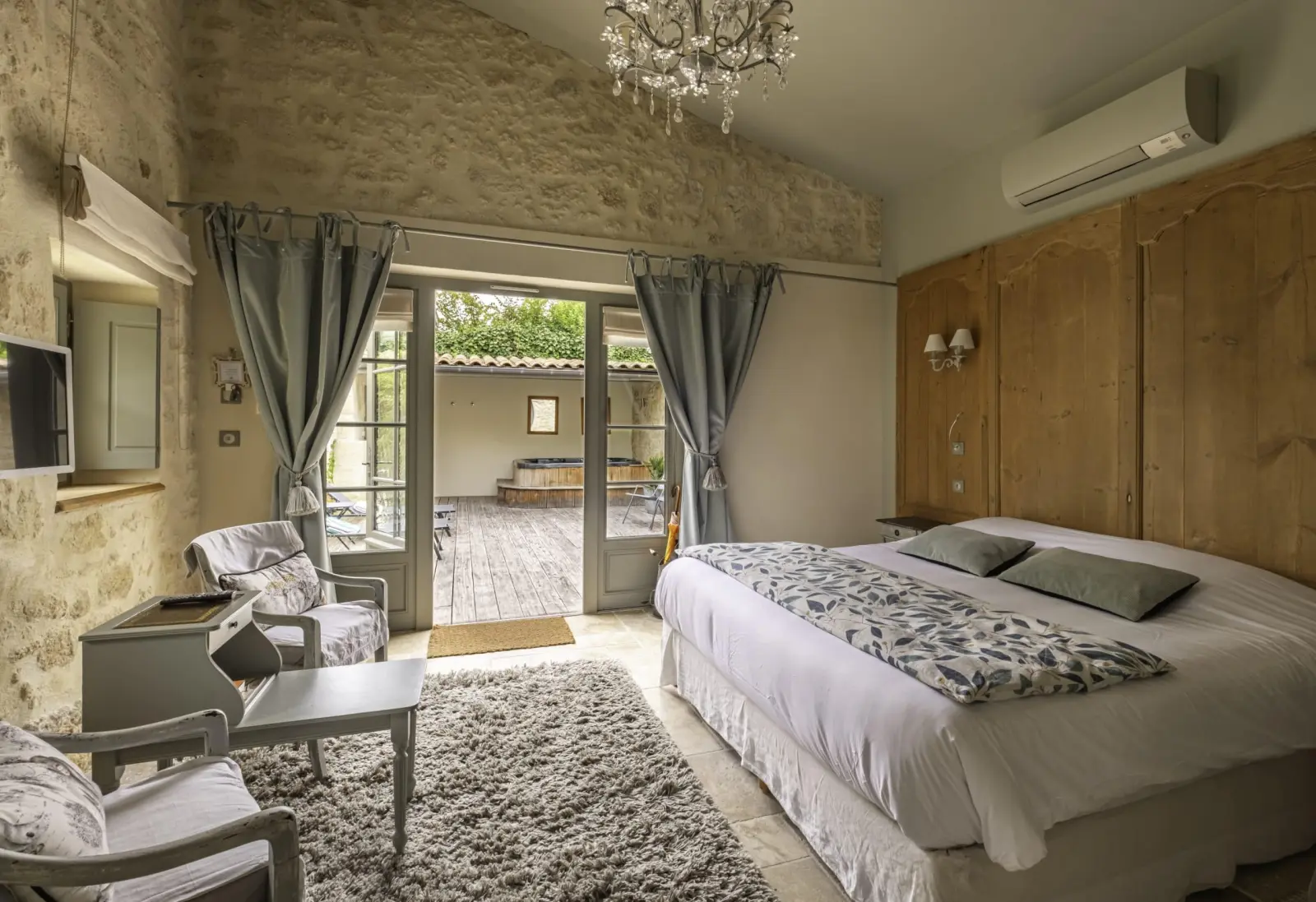 Côté Campagne suite at Clos Marcamps with stone wall, chandelier, panelling and French door onto a wooden deck