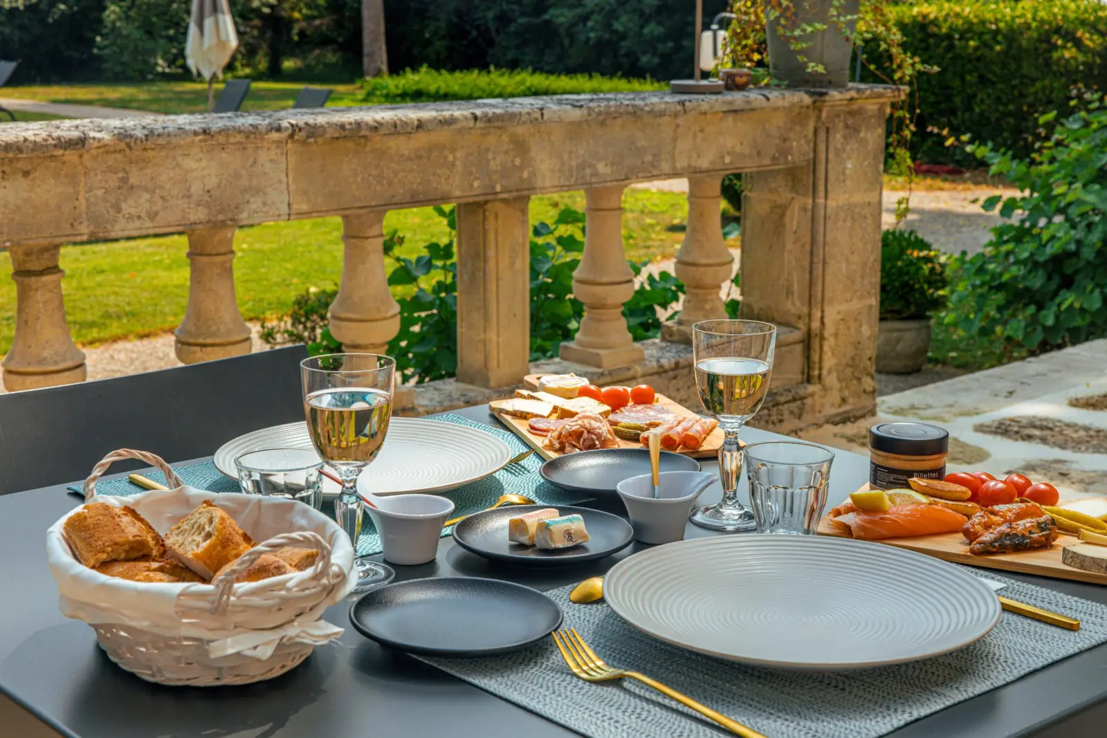 Table set on the terrace at Clos Marcamps with white wine, charcuterie boards and bread, stone balustrade