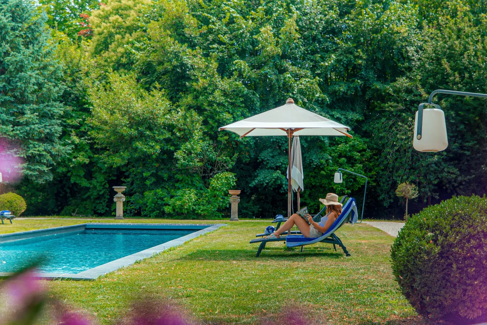 Woman in a hat on a lounger under a parasol beside the pool at Clos Marcamps