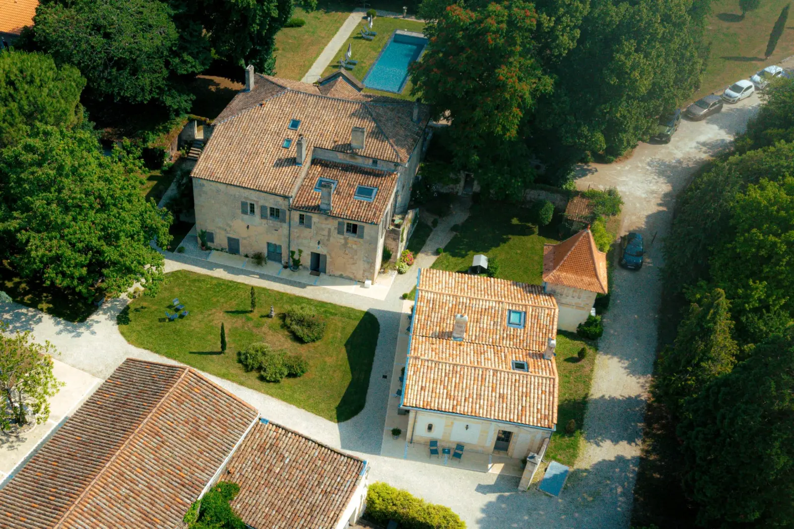 Drone view of Clos Marcamps: tiled-roof buildings, lawns, driveway and the pool beyond