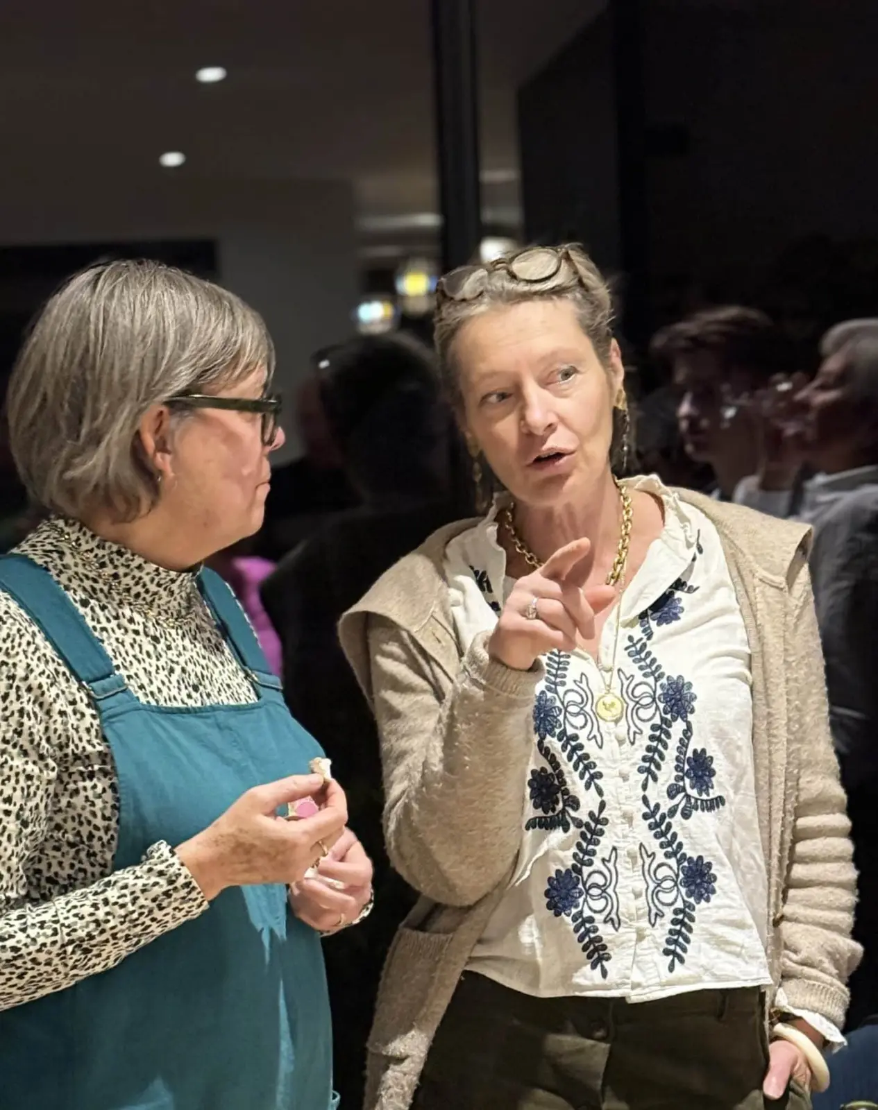 Two women deep in conversation at an evening gathering, one of them pointing