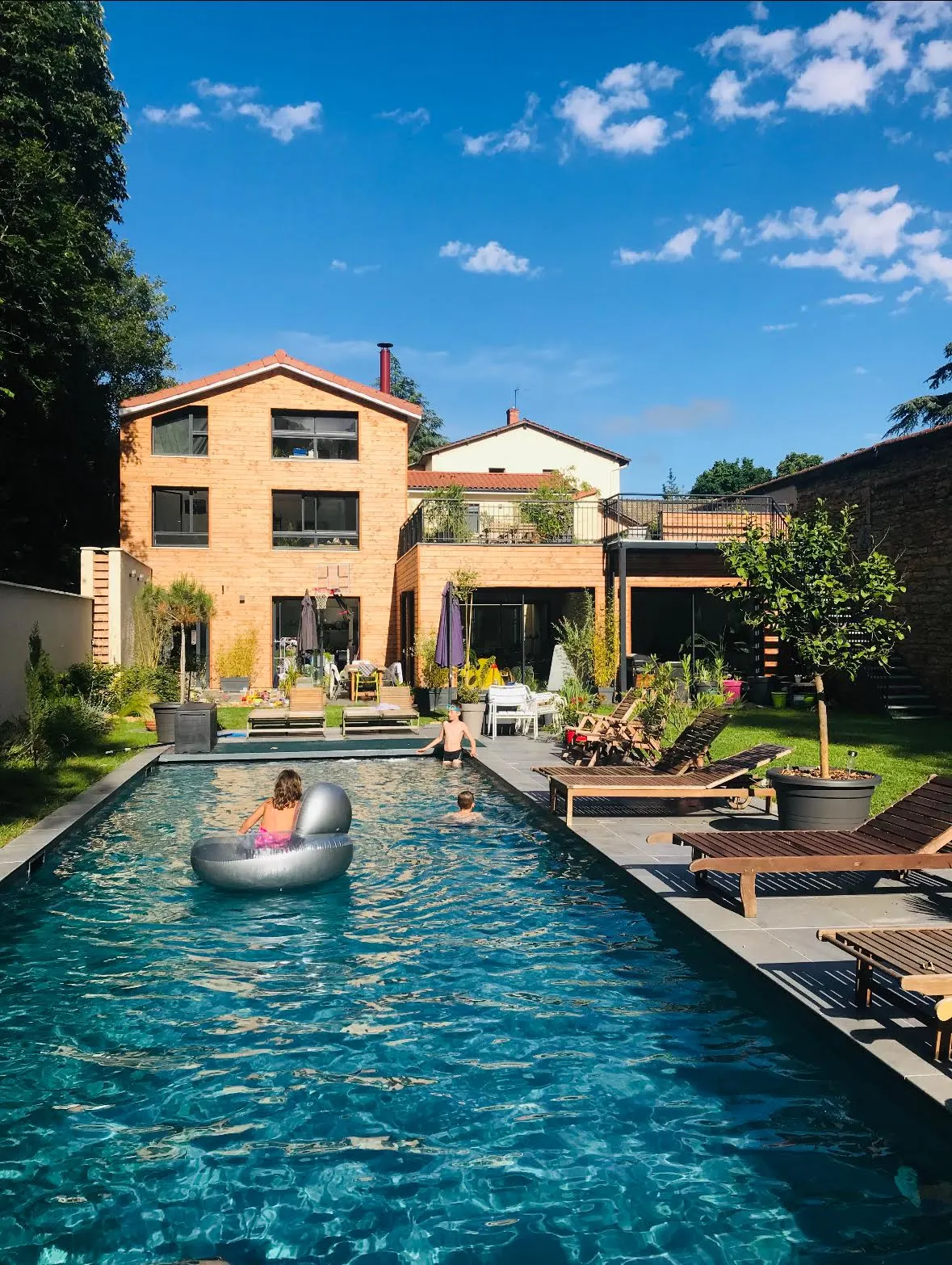 Effet Lodge's large pool with swimmers and a ring float, wooden loungers and the brick house behind