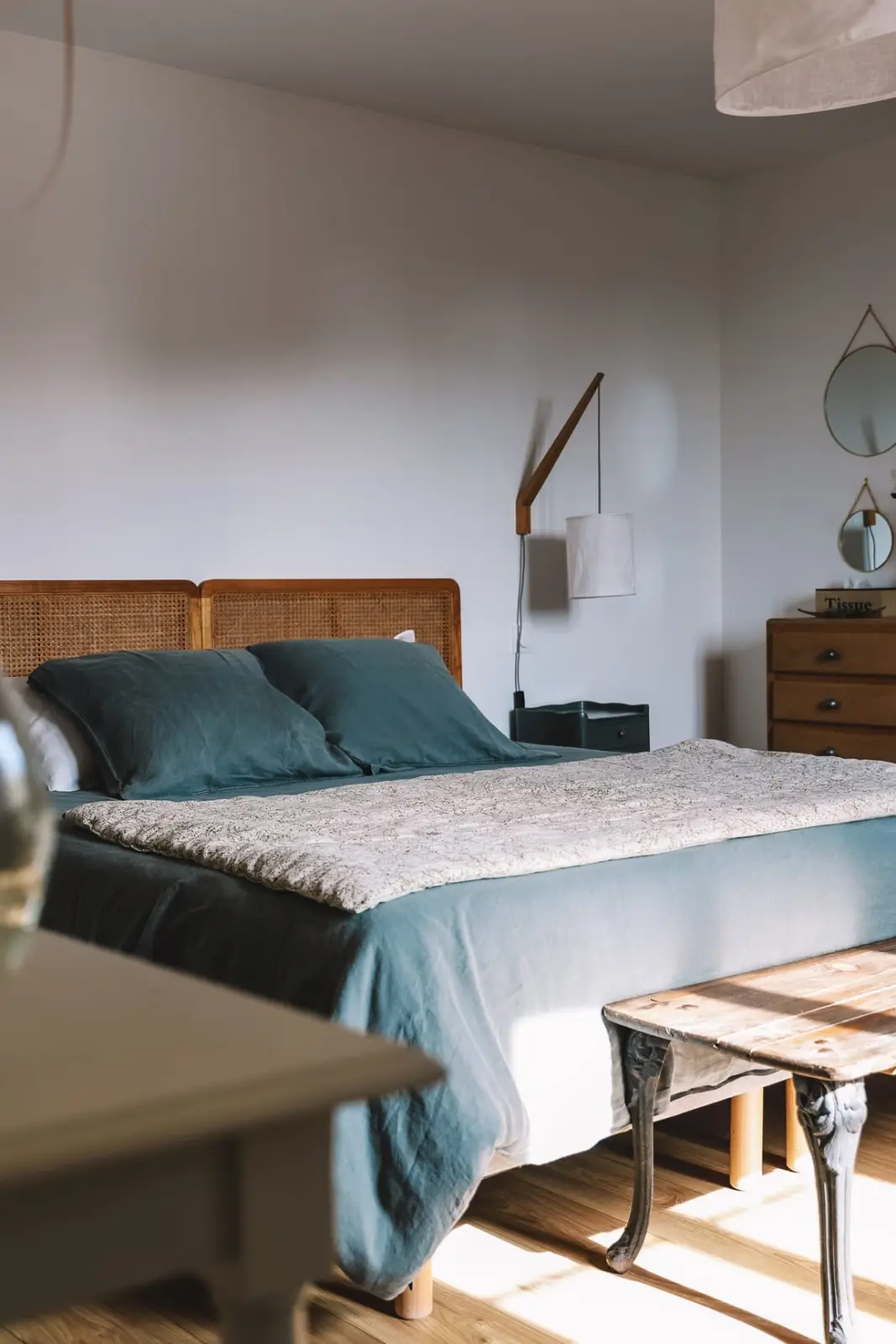 Sunlit bedroom at L'escale Bellifontaine: teal linen bed, cane headboard and wooden bench