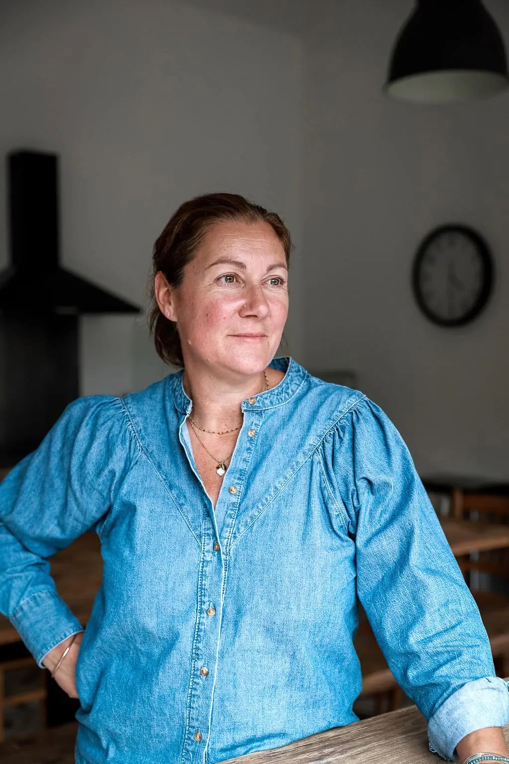 The host of L'Escale Bellifontaine in a denim shirt, leaning on a table in her kitchen
