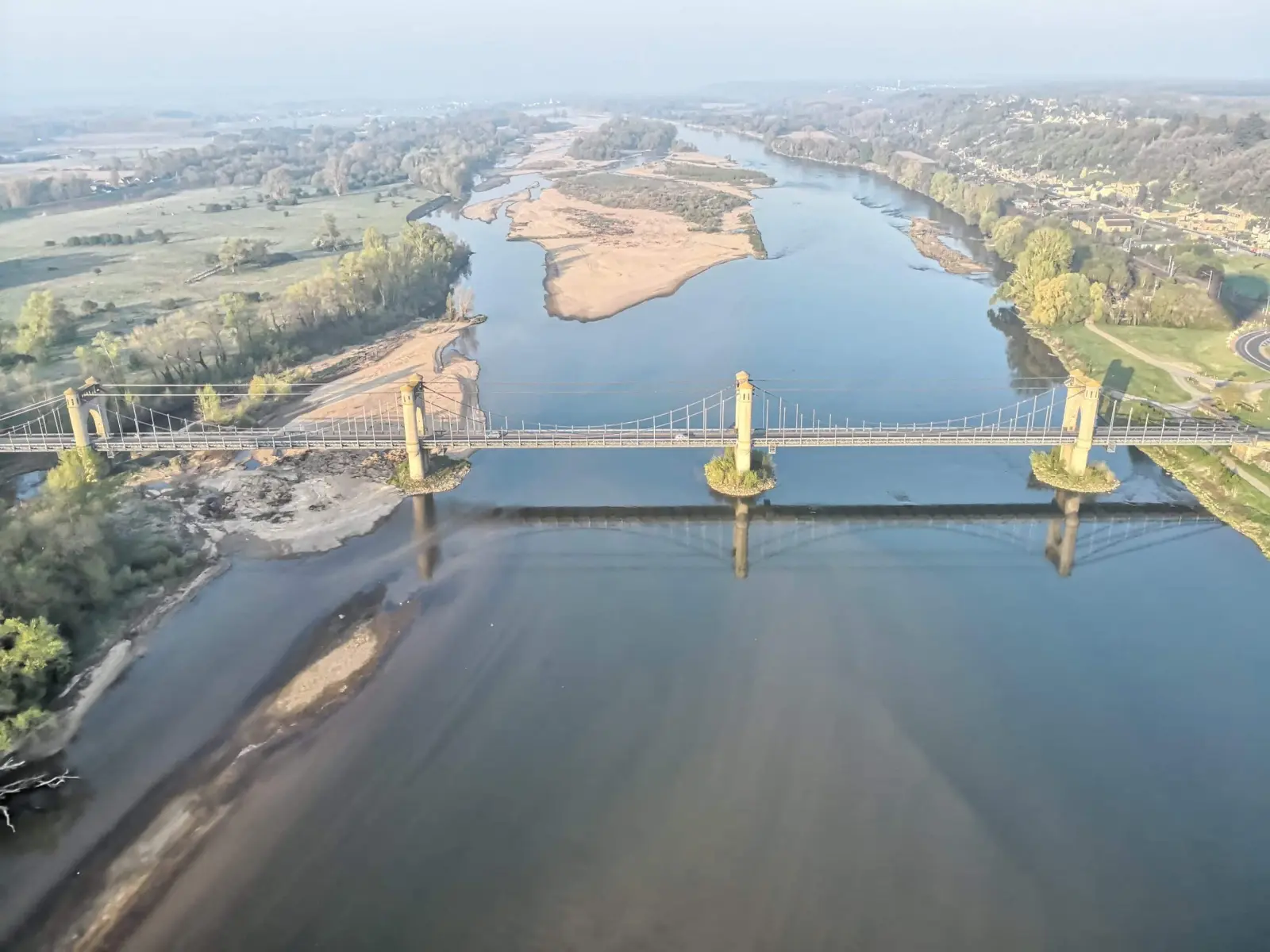Aerial view of a wide river with sandbanks crossed by a suspension bridge, near La Vie Voyage