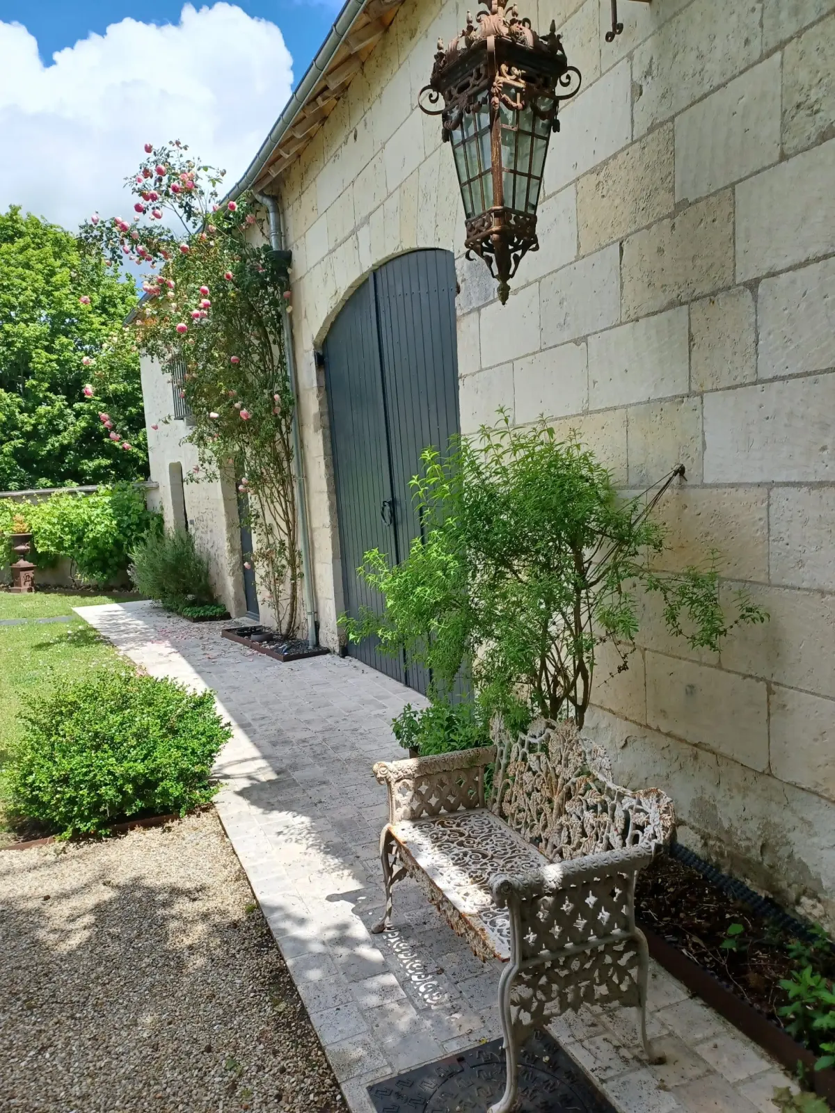 Path along a stone wall with a lantern, grey door and cast-iron bench, La Folie Saint Julien