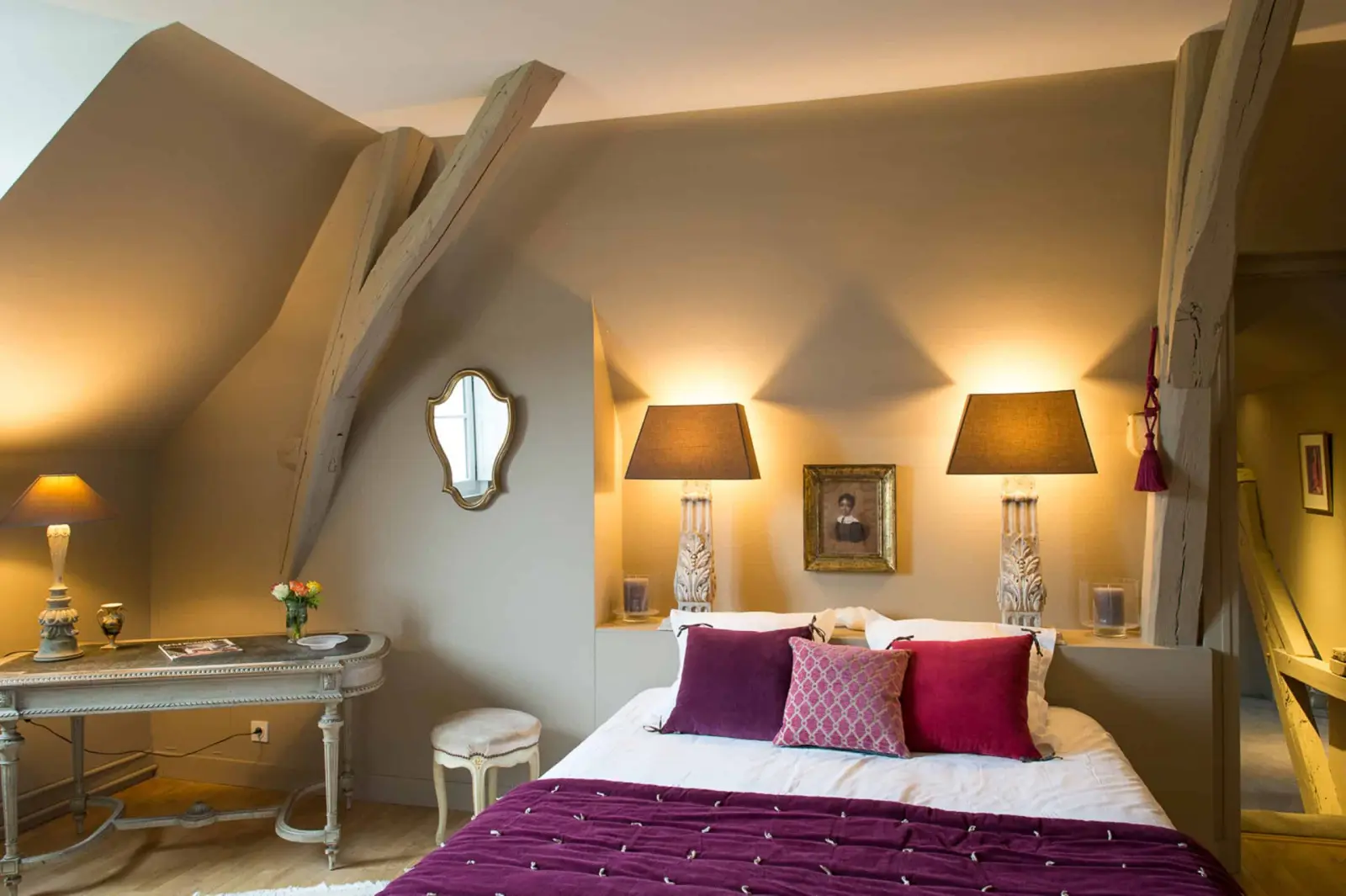 Bedroom under the beams, bed with raspberry and plum cushions, a mirror and a console, La Folie Saint Julien