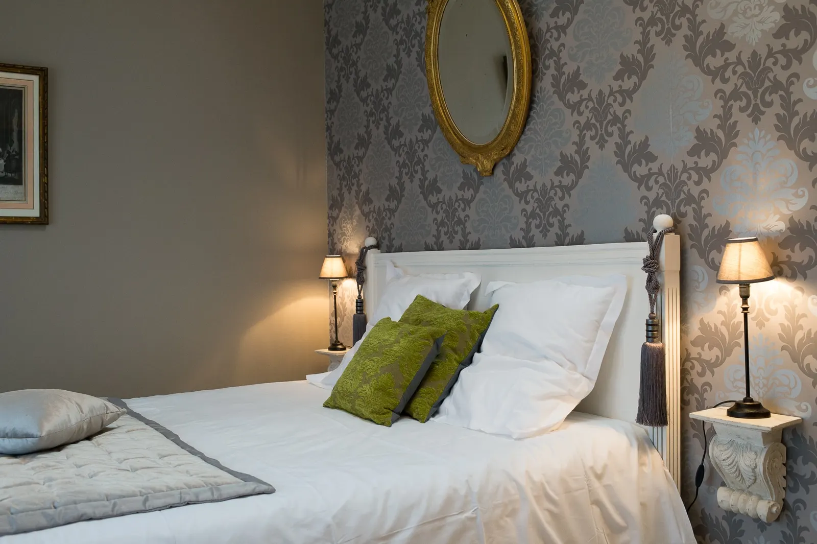 A bedroom at La Folie Saint Julien: white bed, green cushions, grey damask wallpaper and a gilt mirror
