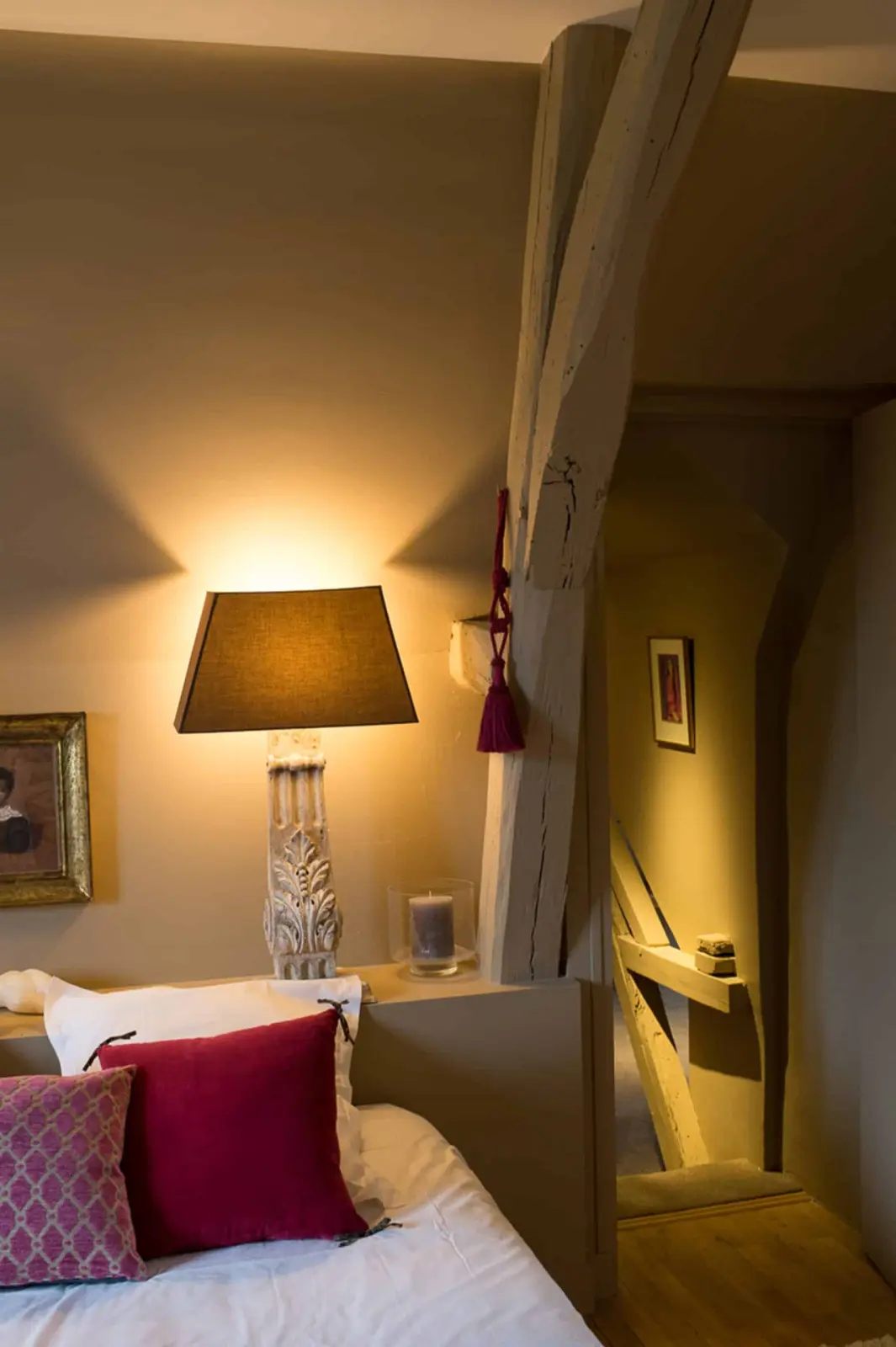A bedroom at La Folie Saint Julien: lit lamp by the bed, raspberry cushions and a weathered timber post