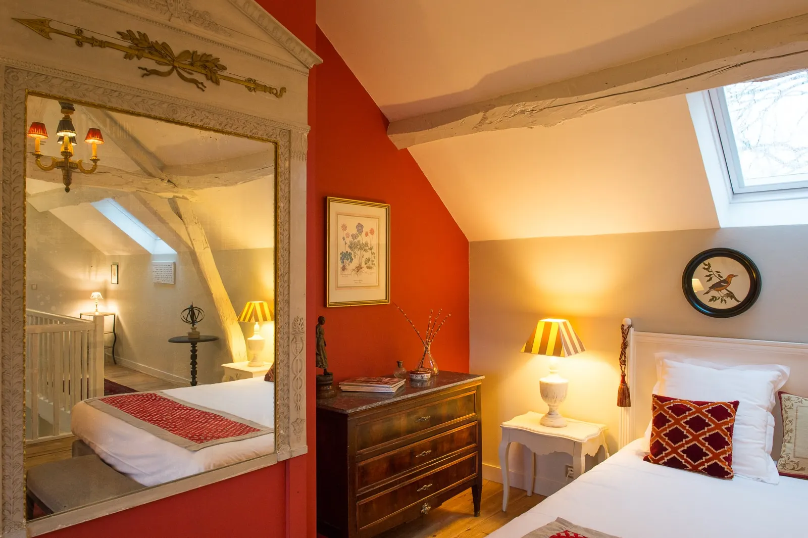 Bedroom with a red wall, large mirror, antique chest of drawers and a bed under a skylight, La Folie Saint Julien