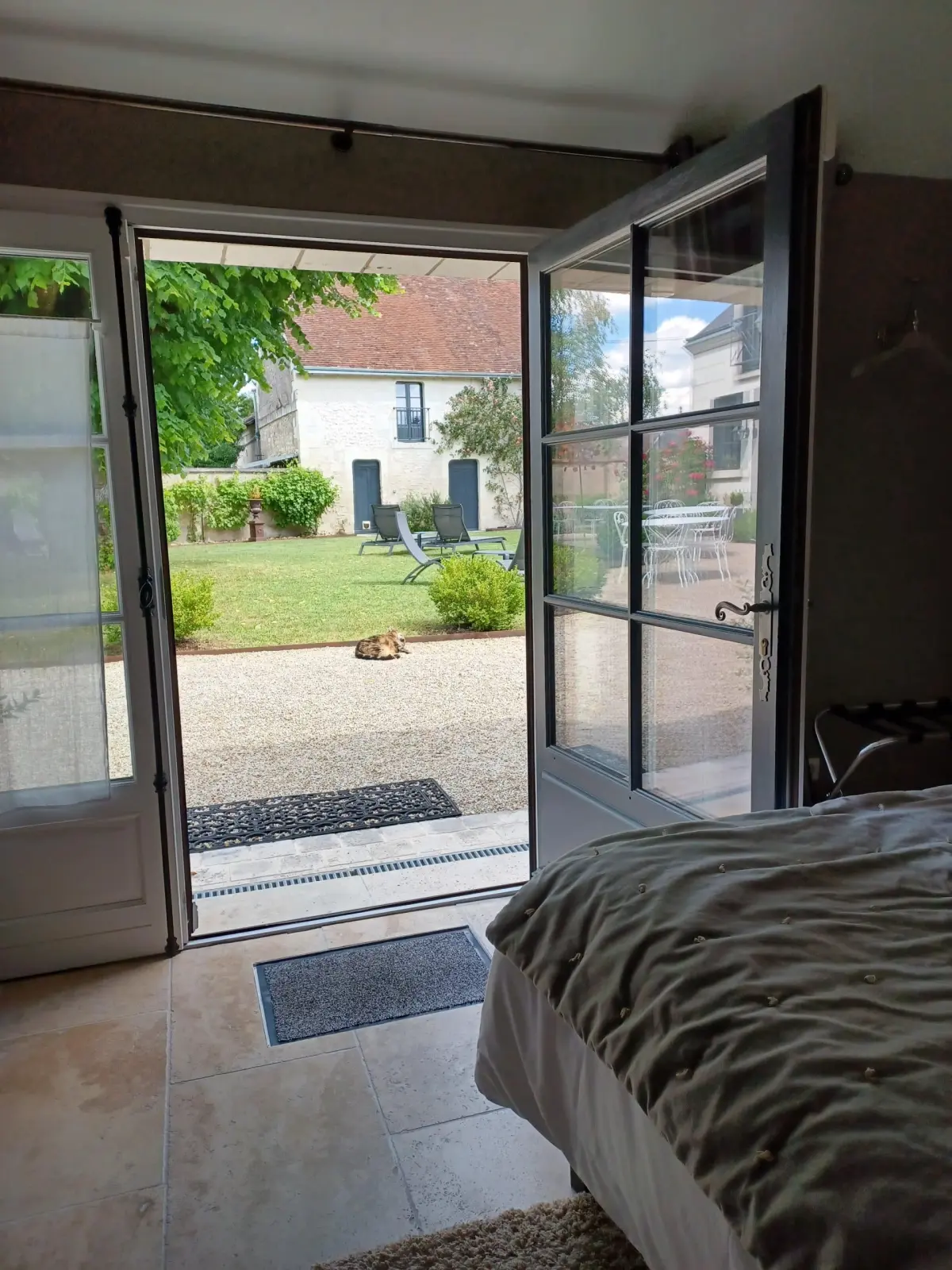 Bedroom with a stone floor, a bed and a French window open onto the courtyard and garden, La Folie Saint Julien