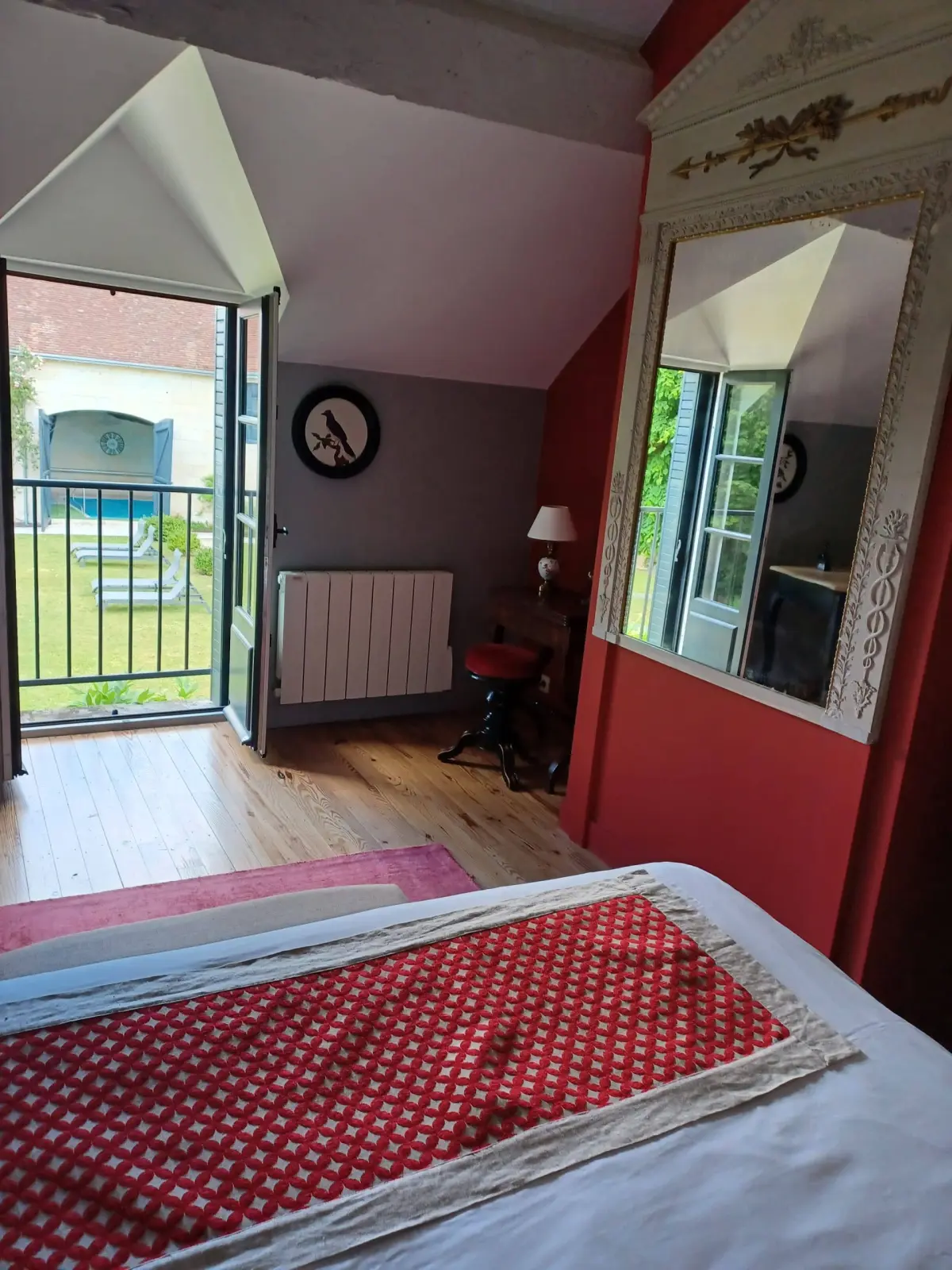 Bedroom with a red wall, a French window open onto the lawn and a large mirror, La Folie Saint Julien