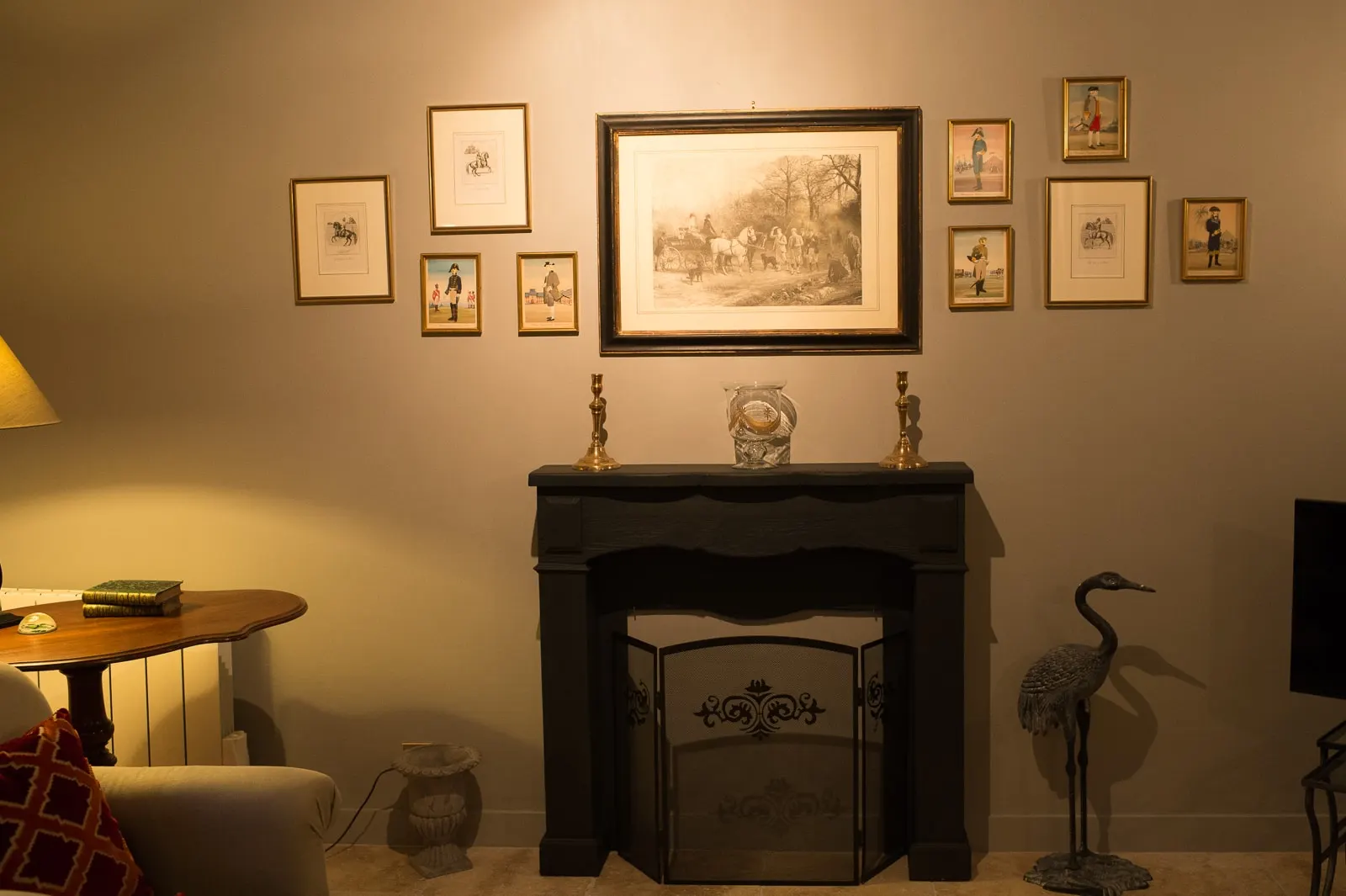 Black fireplace beneath framed prints, with candlesticks and a decorative heron, La Folie Saint Julien